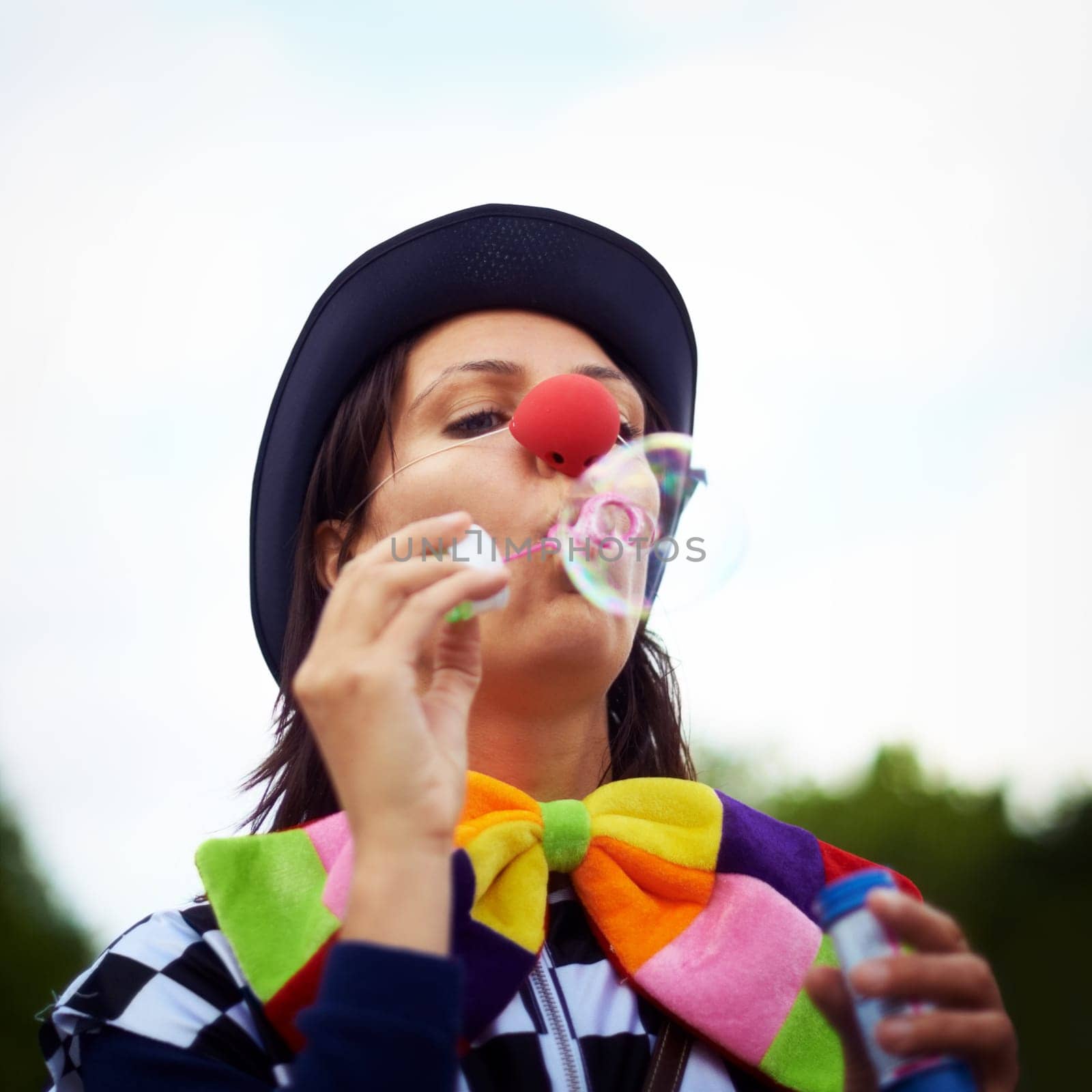 Clown blowing bubbles at outdoor festival for fun, fantasy and summer adventure in nature. Face of person, street performer or circus character in park with creative color at happy carnival event