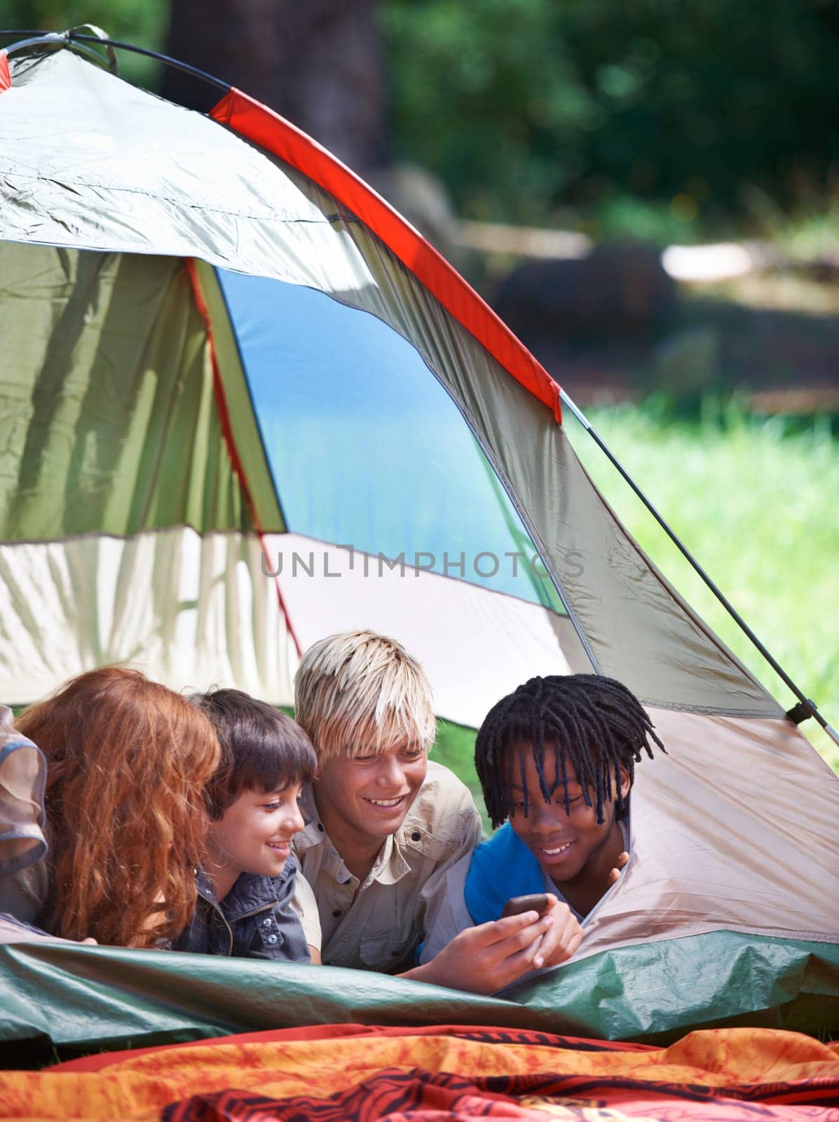 Friends, camping and happy of children in tent for resting, relaxing and bonding with cellphone. Travel gear, smile and young girls and boys for adventure on holiday, vacation and weekend outdoors.