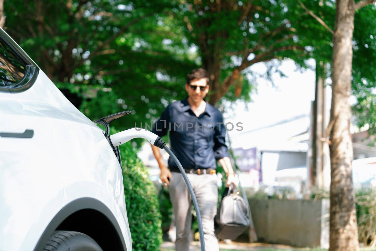 Young man recharge electric car's battery from charging station. Expedient by biancoblue