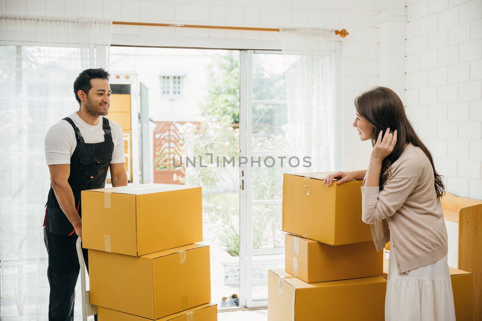 Professional movers aid couple indoors unloading boxes from truck into the home. Service guarantees customer satisfaction during relocation. Teamwork and efficient assistance portrayed. Moving day