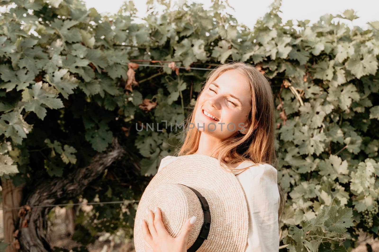 Woman at autumn winery. Portrait of happy woman holding glass of wine and enjoying in vineyard. Elegant young lady in hat toasting with wineglass smiling cheerfully enjoying her stay at vineyard