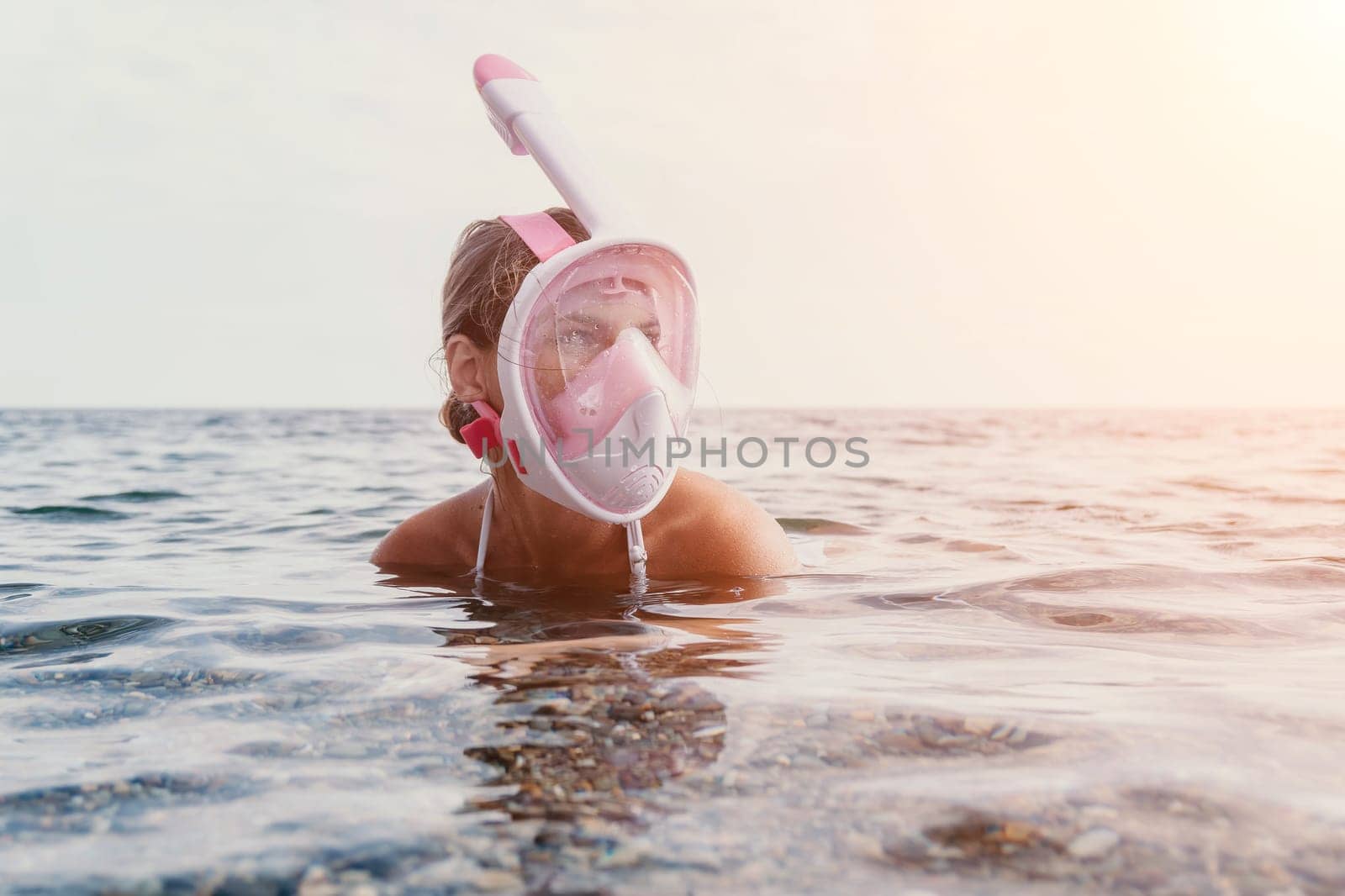 Young happy woman in white bikini and wearing pink mask gets ready for sea snorkeling. Positive smiling woman relaxing and enjoying water activities with family summer travel holidays vacation on sea. by panophotograph