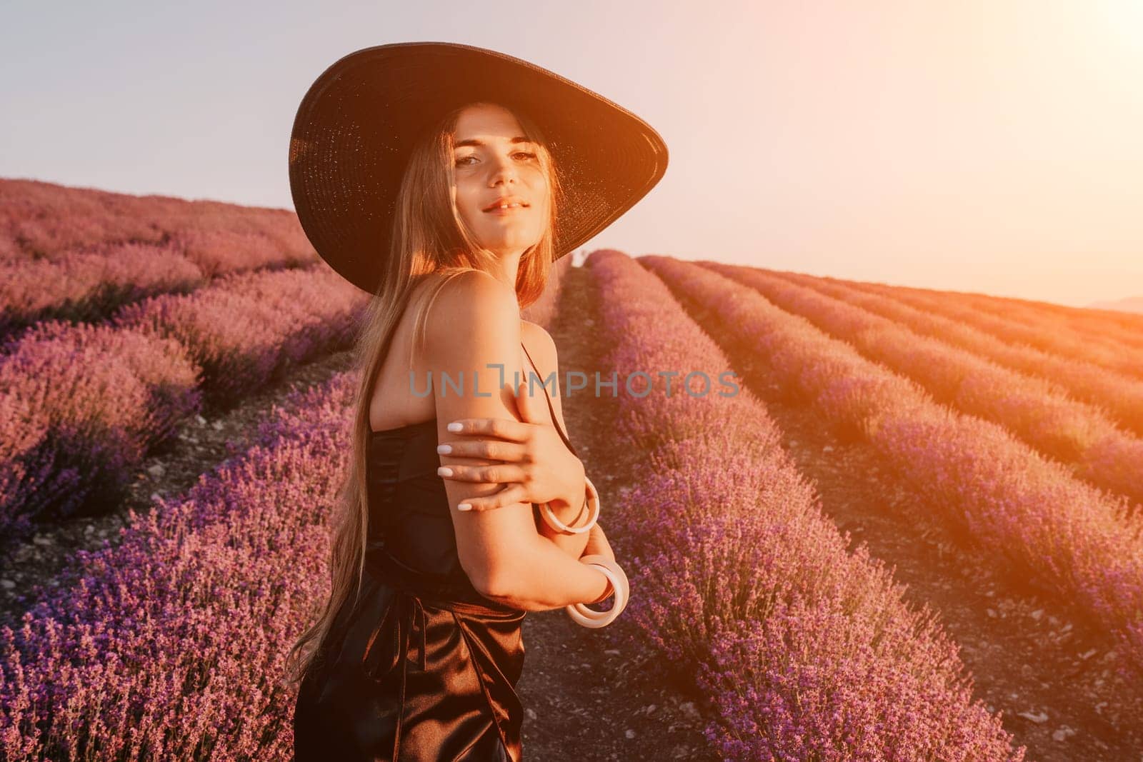 Close up portrait of young beautiful woman in a white dress and a hat is walking in the lavender field and smelling lavender bouquet.