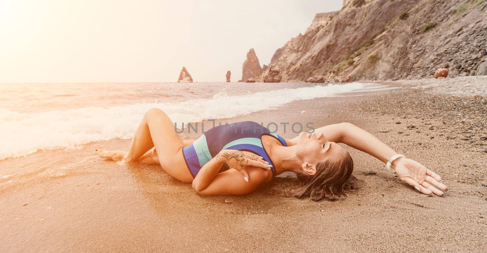 Woman summer travel sea. Happy tourist in blue bikini enjoy taking picture outdoors for memories. Woman traveler posing on the beach surrounded by volcanic mountains, sharing travel adventure journey by panophotograph