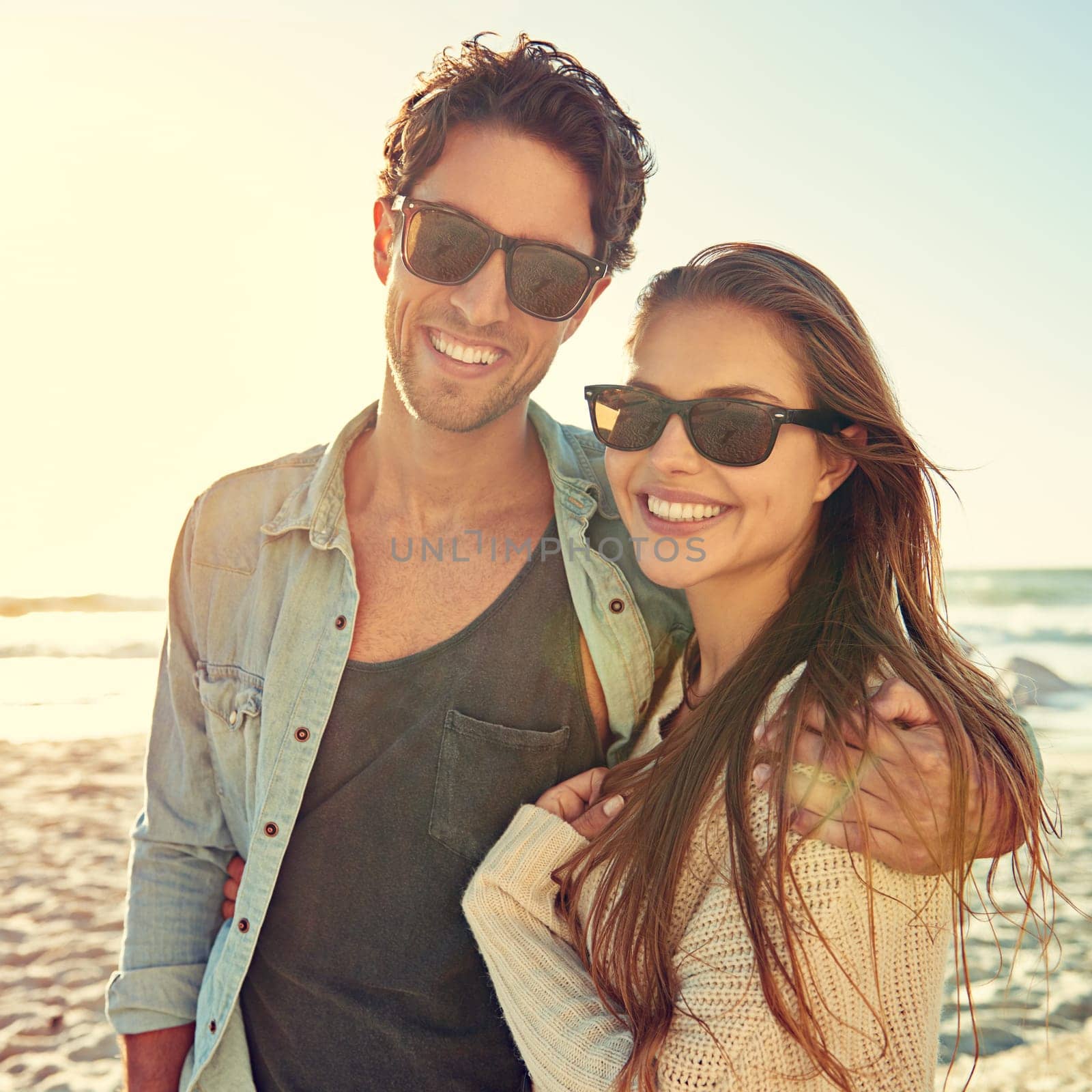 Couple, ocean and sunglasses with hug, smile or care for fashion, eye protection or vacation in summer. Man, woman and embrace in glasses at beach for sun, happy or love by waves on tropical holiday.