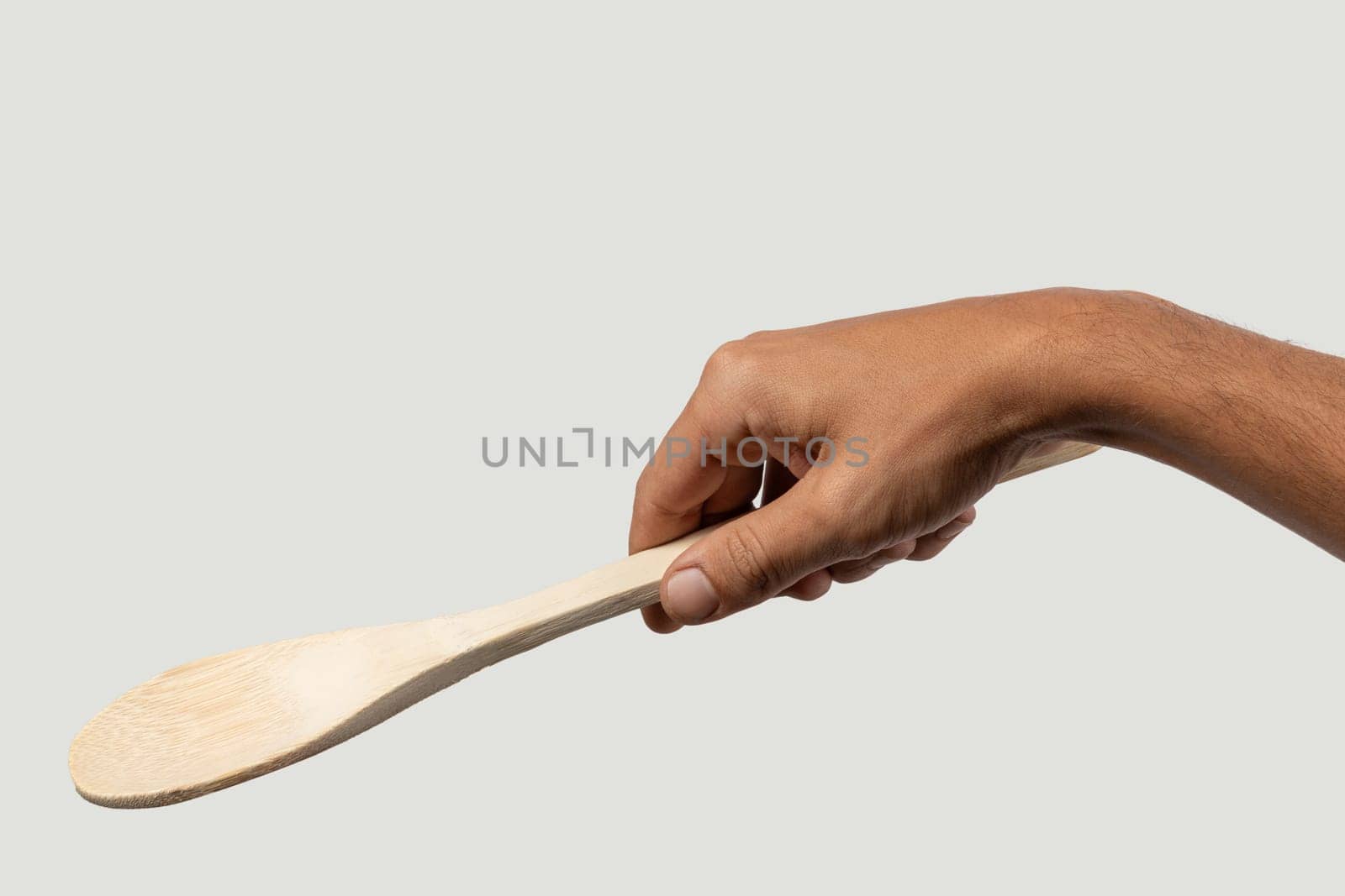 Black male hand holding a wooden cooking spoon on grey background. High quality photo