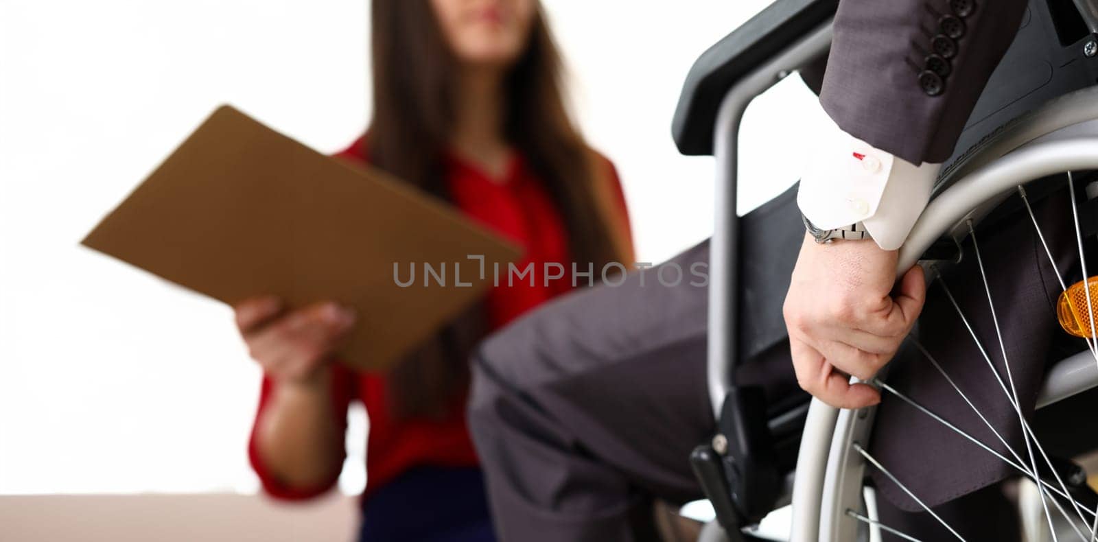 Man in suit on wheelchair communicates with woman. Prestigious job for people with disabilities. Office has working conditions for disabled. Active employment people with disabilities