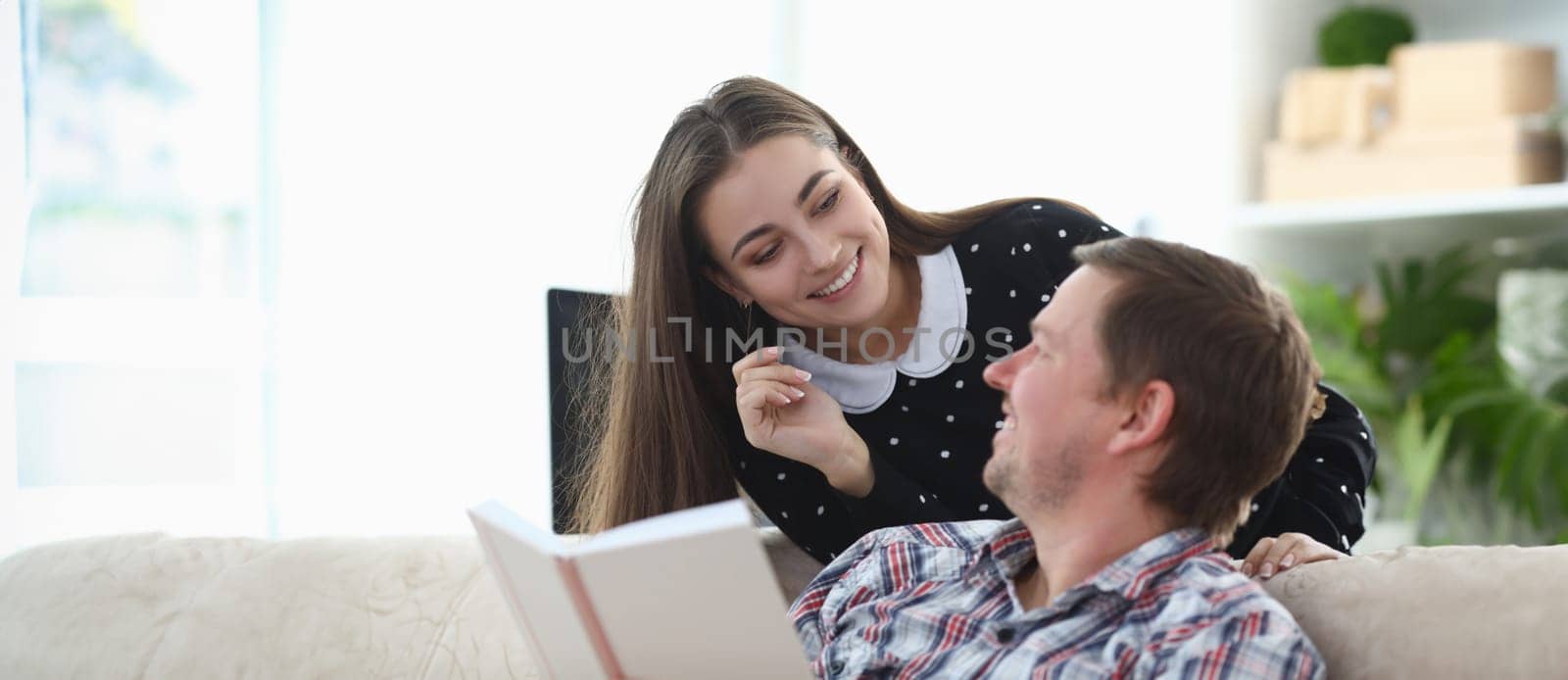 Guy is sitting on couch with book, girl is smiling by kuprevich