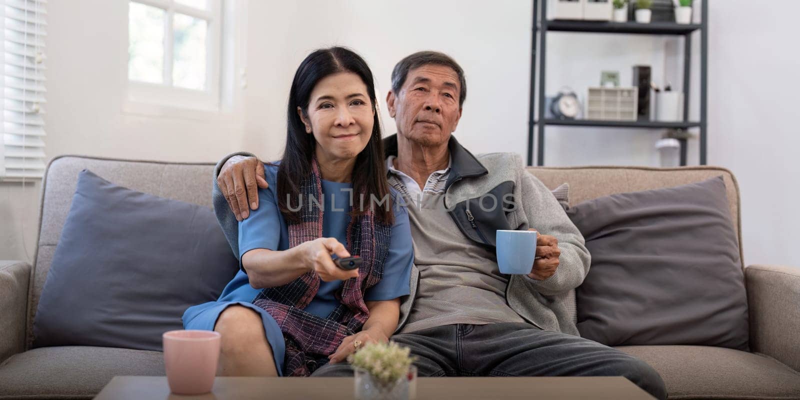 Senior couple watching tv and sofa in relax for movie or series in living room at home. Elderly man and woman with coffee and remote together for changing channel and online entertainment by nateemee