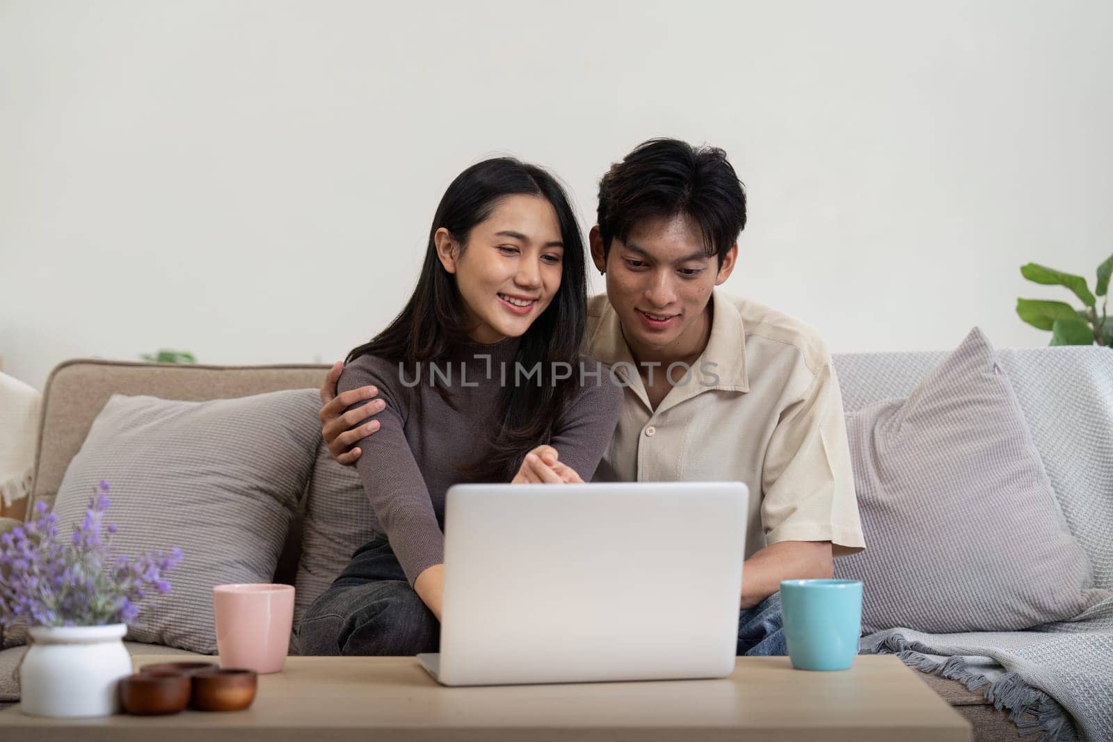 Young couple asian using laptop together while sitting on sofa at home by nateemee