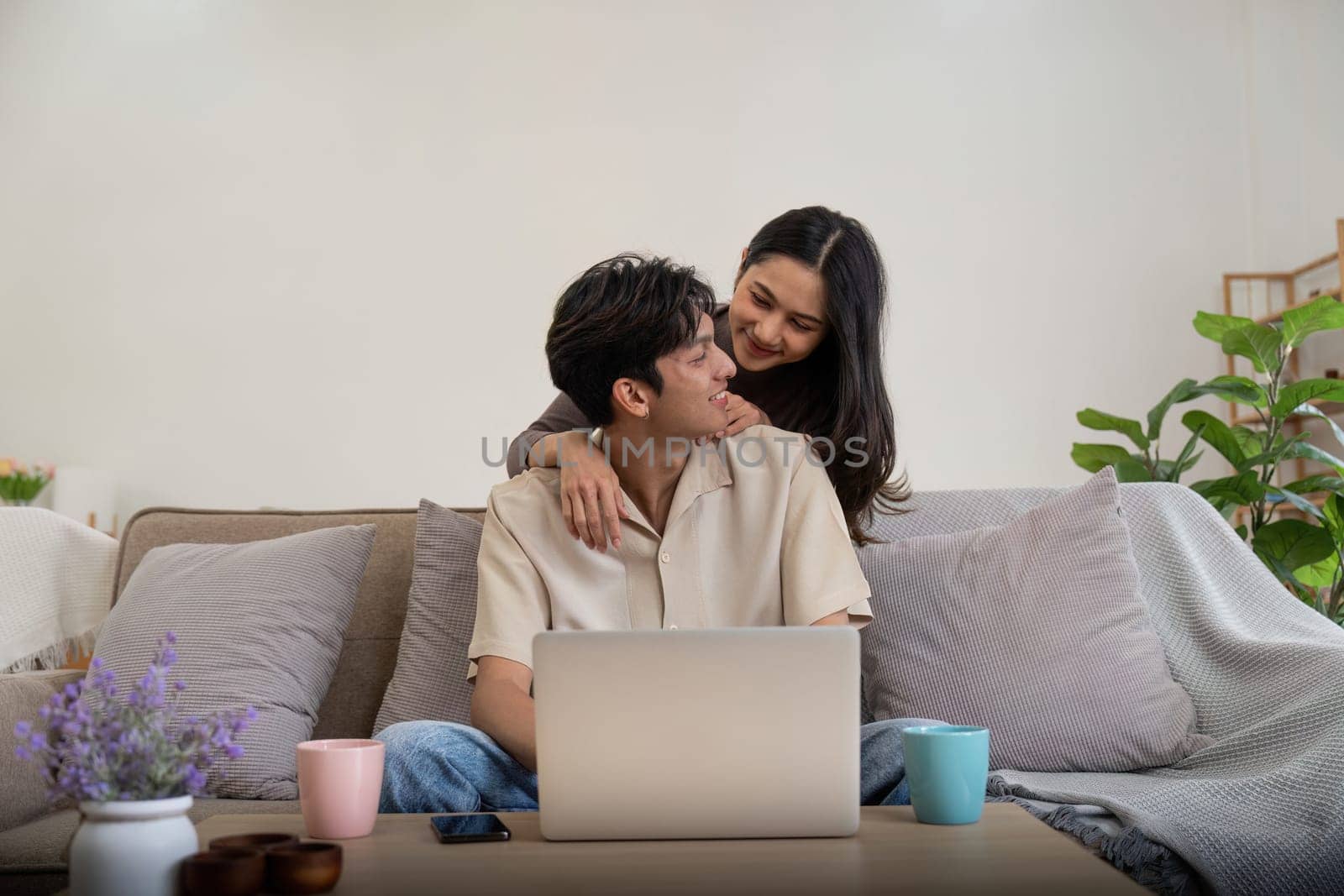 Young couple asian using laptop together while sitting on sofa at home.