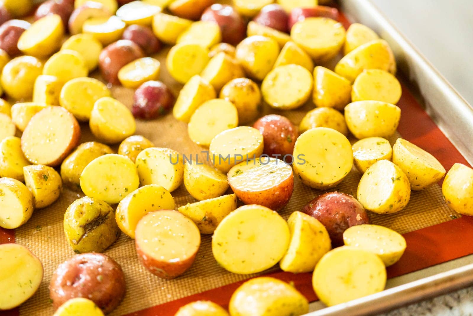 In a modern kitchen, an array of halved, multicolored marble potatoes are arranged on a baking pan lined with a silicone liner. The roasting process infuses the kitchen with a mouthwatering aroma, indicating a delicious side dish in the making.