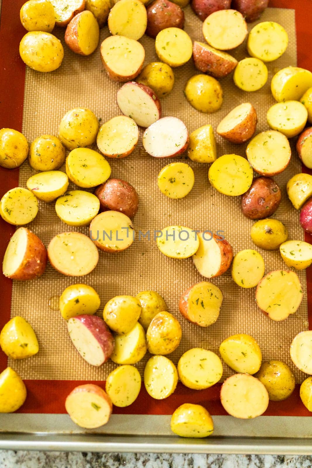 In a modern kitchen, an array of halved, multicolored marble potatoes are arranged on a baking pan lined with a silicone liner. The roasting process infuses the kitchen with a mouthwatering aroma, indicating a delicious side dish in the making.