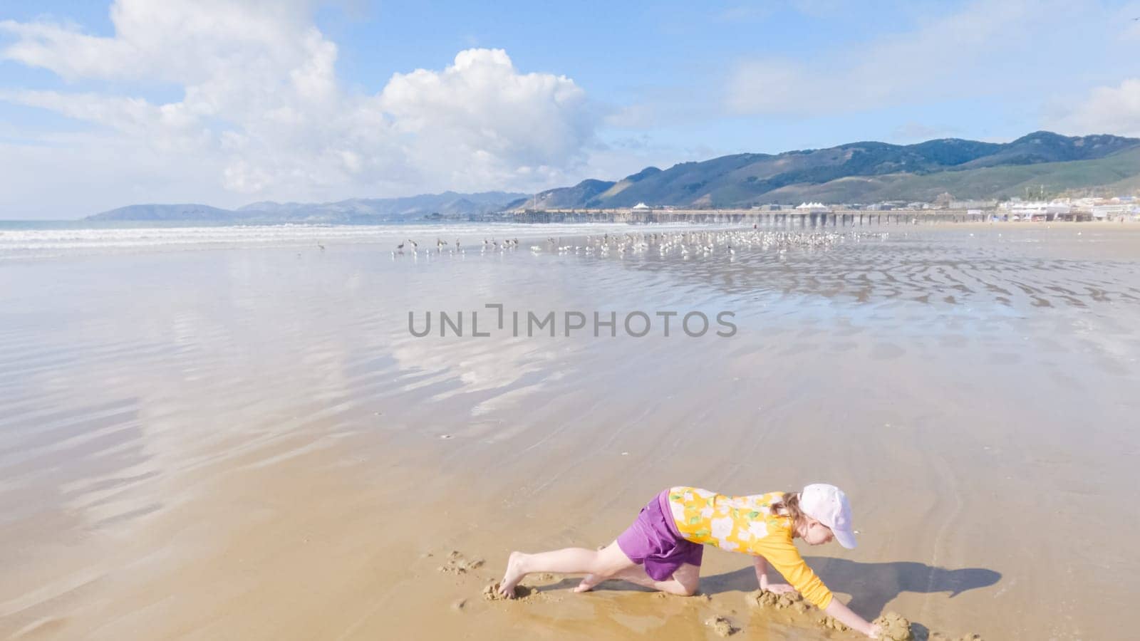 Little girl joyfully clamming on Pismo Beach, bundled up for the winter chill as she explores the sands for seashells and clams.