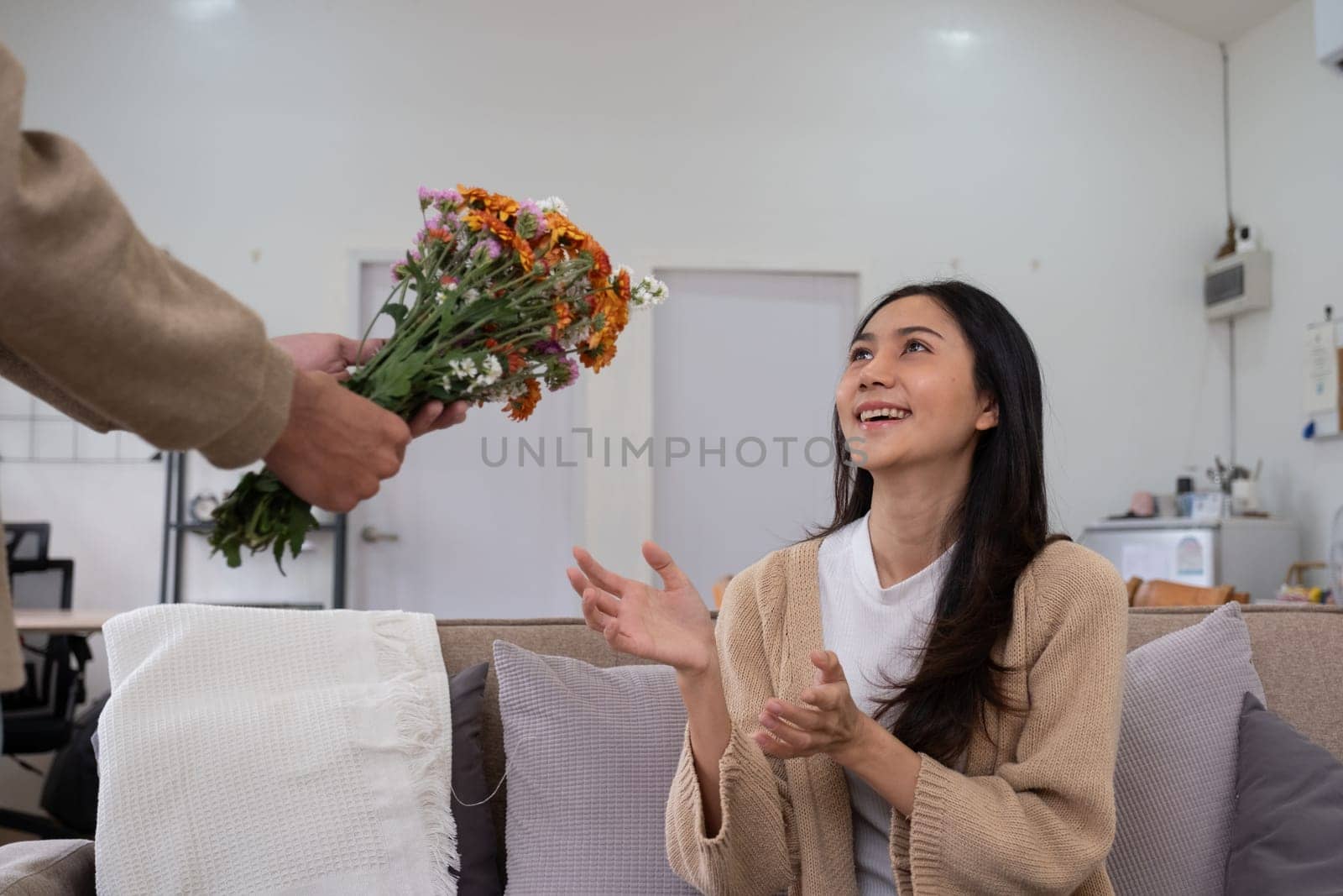 Romantic young asian couple embracing with holding flowers and smiling in living room at home. fall in love. Valentine concept.