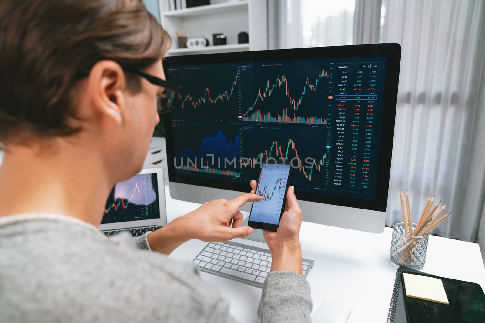 Smart stock investors pointing on screen with smartphone for market stock exchange along with laptop screen in highest dynamic investment rate, focusing data planning at modern workplace. Pecuniary.