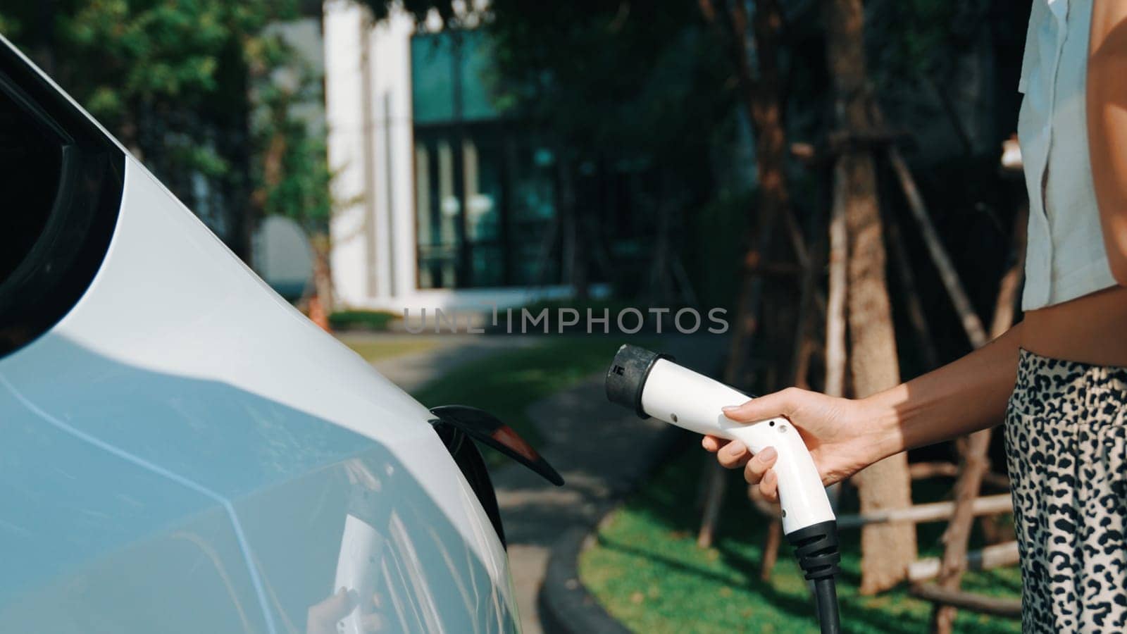 Young woman recharge EV electric car battery at residential area EV charging station in smart home with sustainable green renewable clean energy lifestyle for electric vehicle urban commute innards