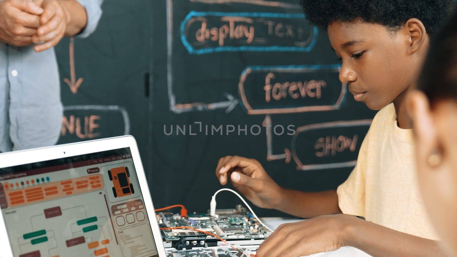 Cute african boy learning to use electronic tool while laptop display code while teacher talking about writing engineering prompt. Diverse children coding program to fixing car model. Edification.