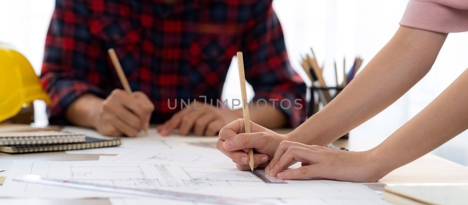 Cropped image of cooperative architect team decide and work together on meeting table with house model, safety helmet and architectural plan scatter around. Closeup. Focus on hand. Burgeoning.