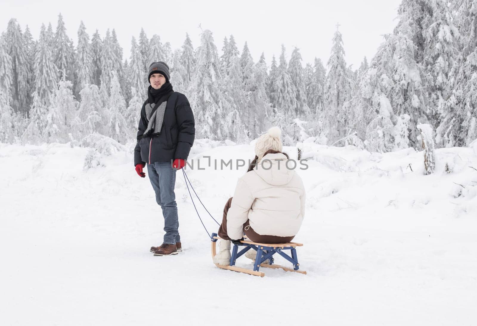 A young handsome caucasian guy is standing resting after sledding his girlfriend in a snowy winter forest in a nature reserve in Belgium, close-up side view. Winter holidays concept.