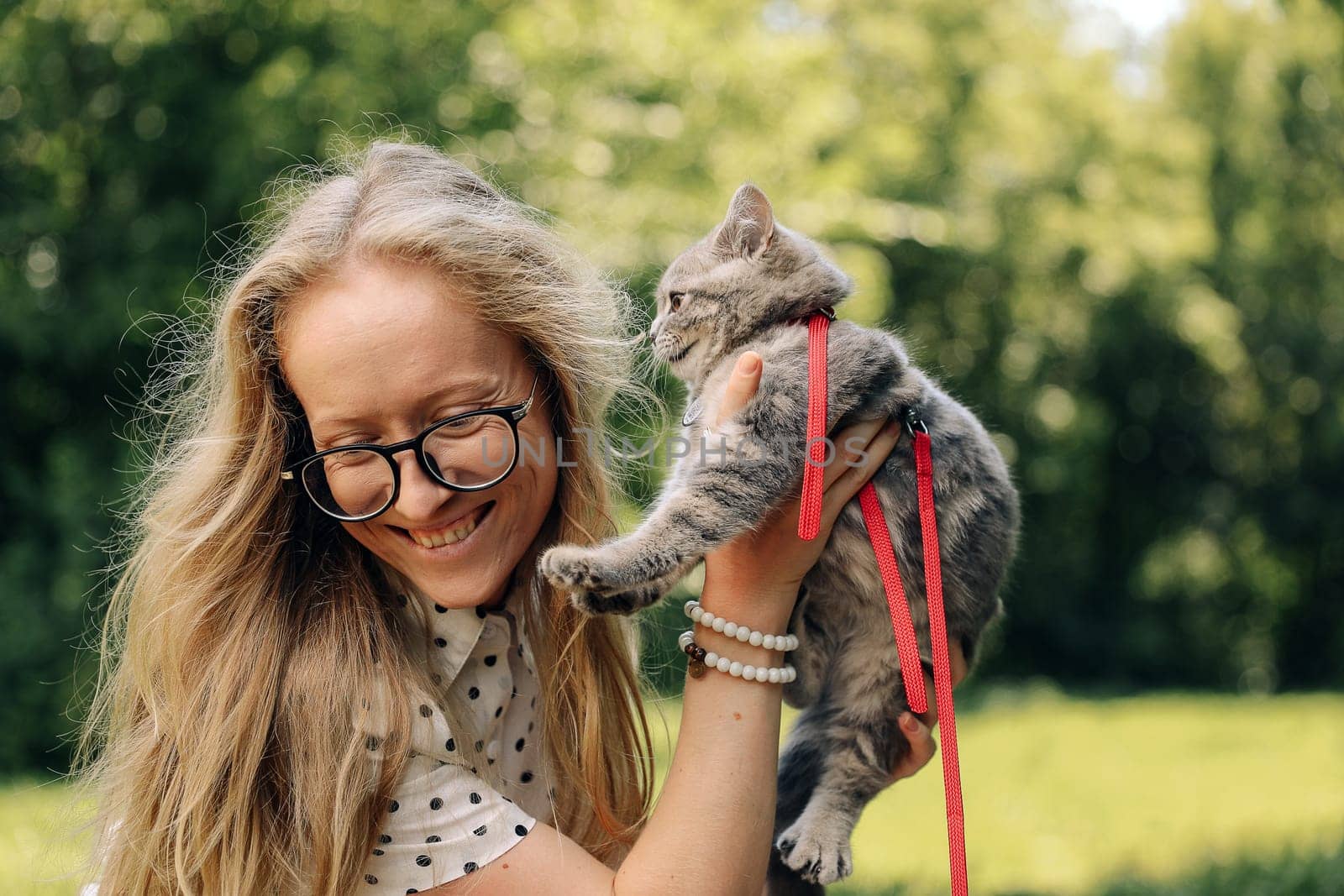 A young blonde woman holds a Scottish straight kitten and smiles
