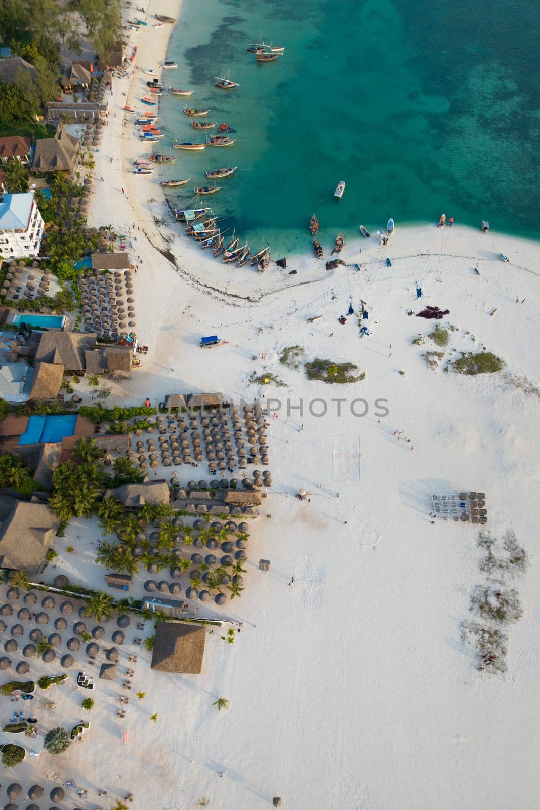 Aerial view of the fishing boats and umbrellas on tropical sea coast with sandy beach.Summer travel in Zanzibar, Africa.Top view of boats and clear green water.