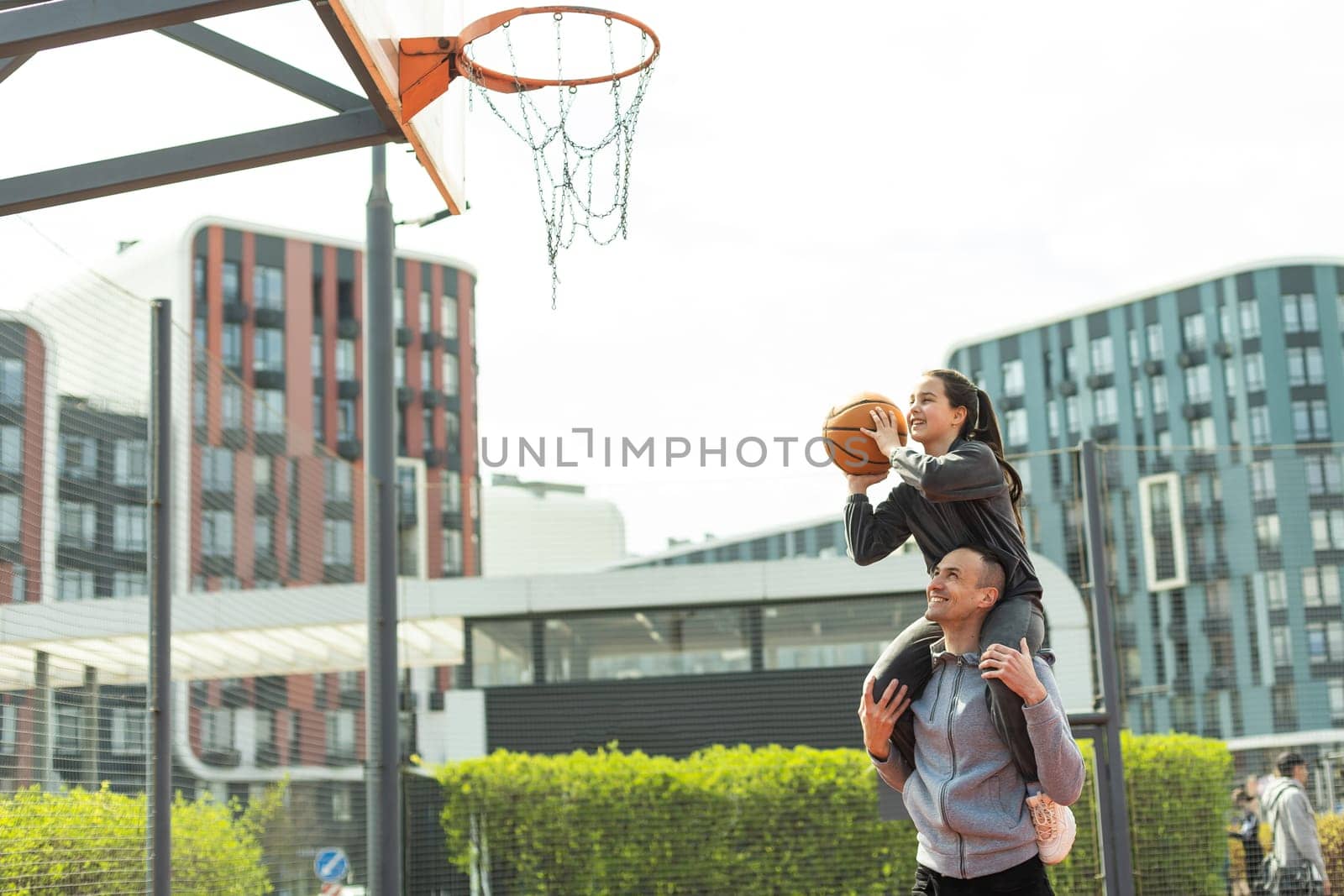 Happy father and teen daughter outside at basketball court. by Andelov13