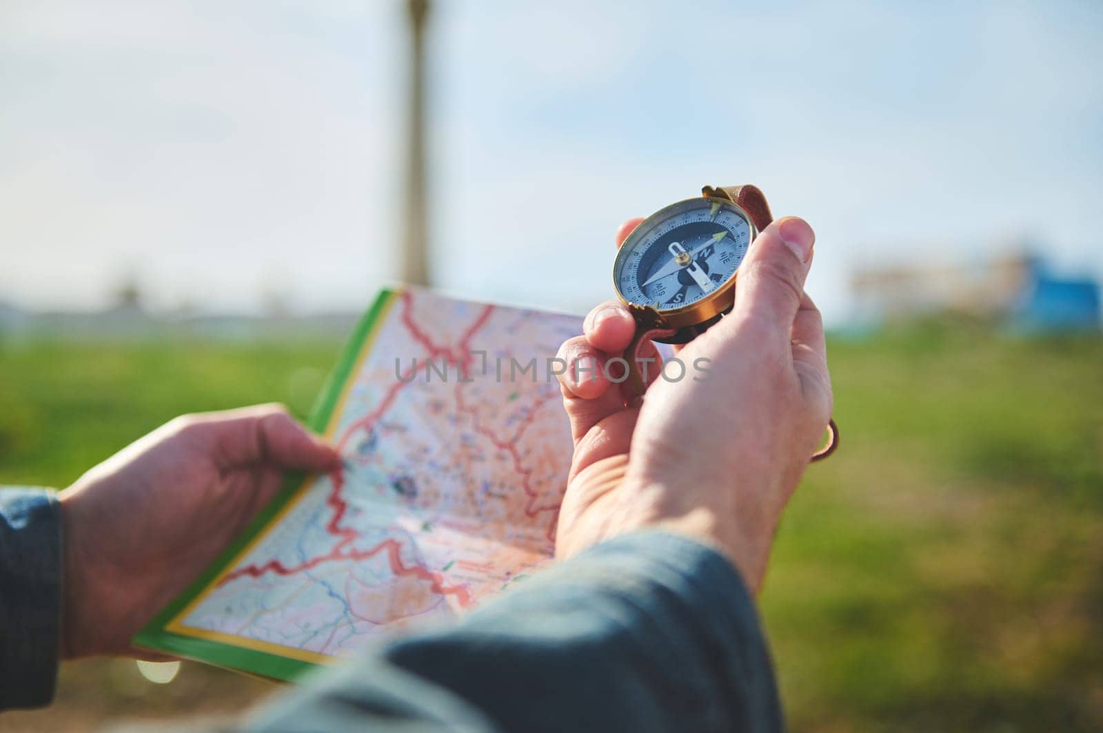 Male hand holds compass with magnetic arrow showing north direction, over a map while discovers a new travel destination by artgf