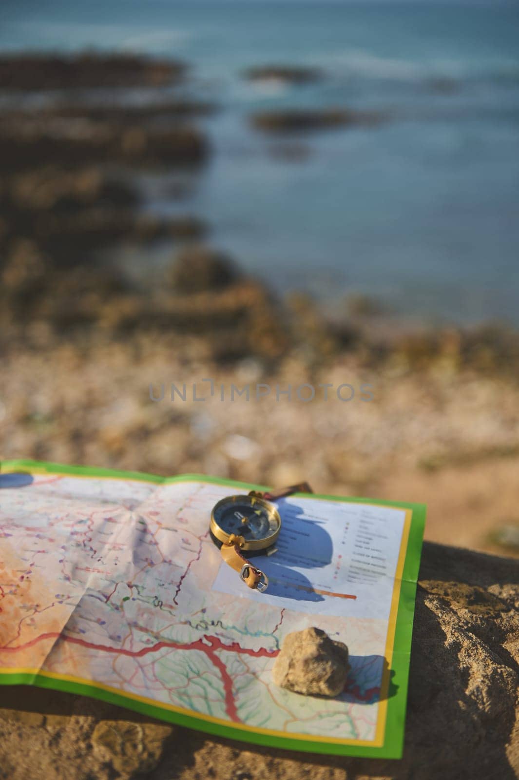 Close-up of an old golden compass and geographic map on a rock over seascape background. Trip. Tourism. Travel concept. by artgf