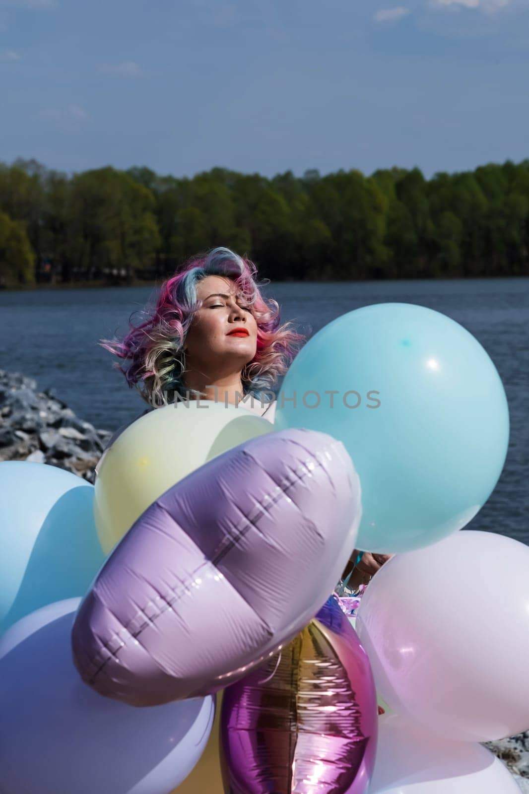 Woman in colored hair walks with an armful of balloons and drinks a refreshing beverage.