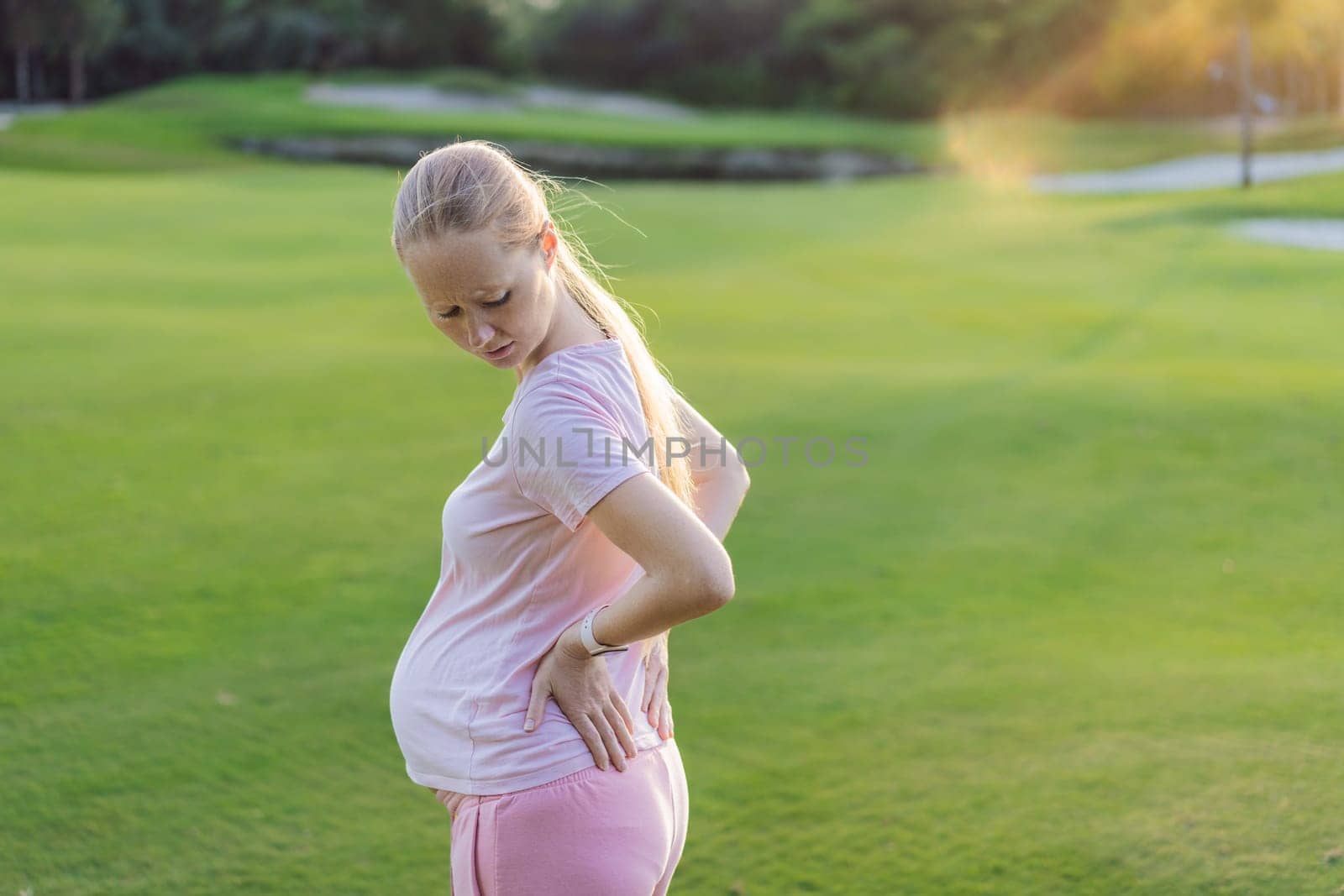 Expectant woman experiences back pain outdoors, seeking relief and comfort during pregnancy with a gentle outdoor stretch or rest by galitskaya