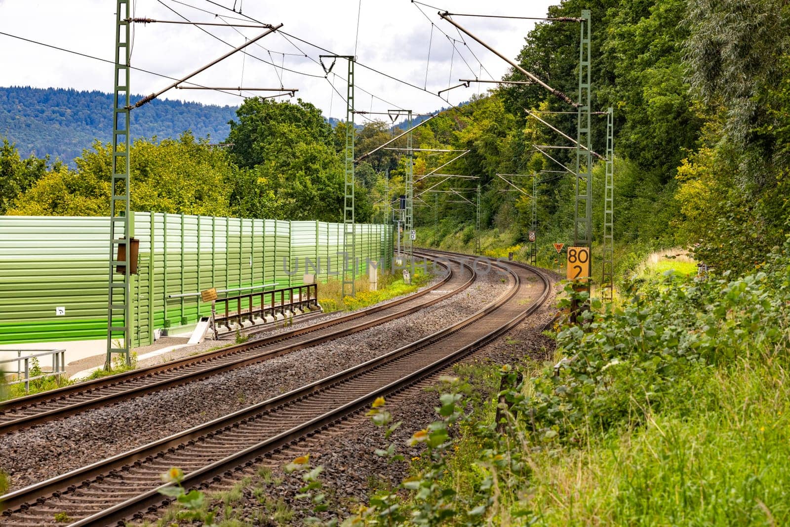 Two parallel tracks of a railroad line run next to a noise barrier through rural Bavaria
