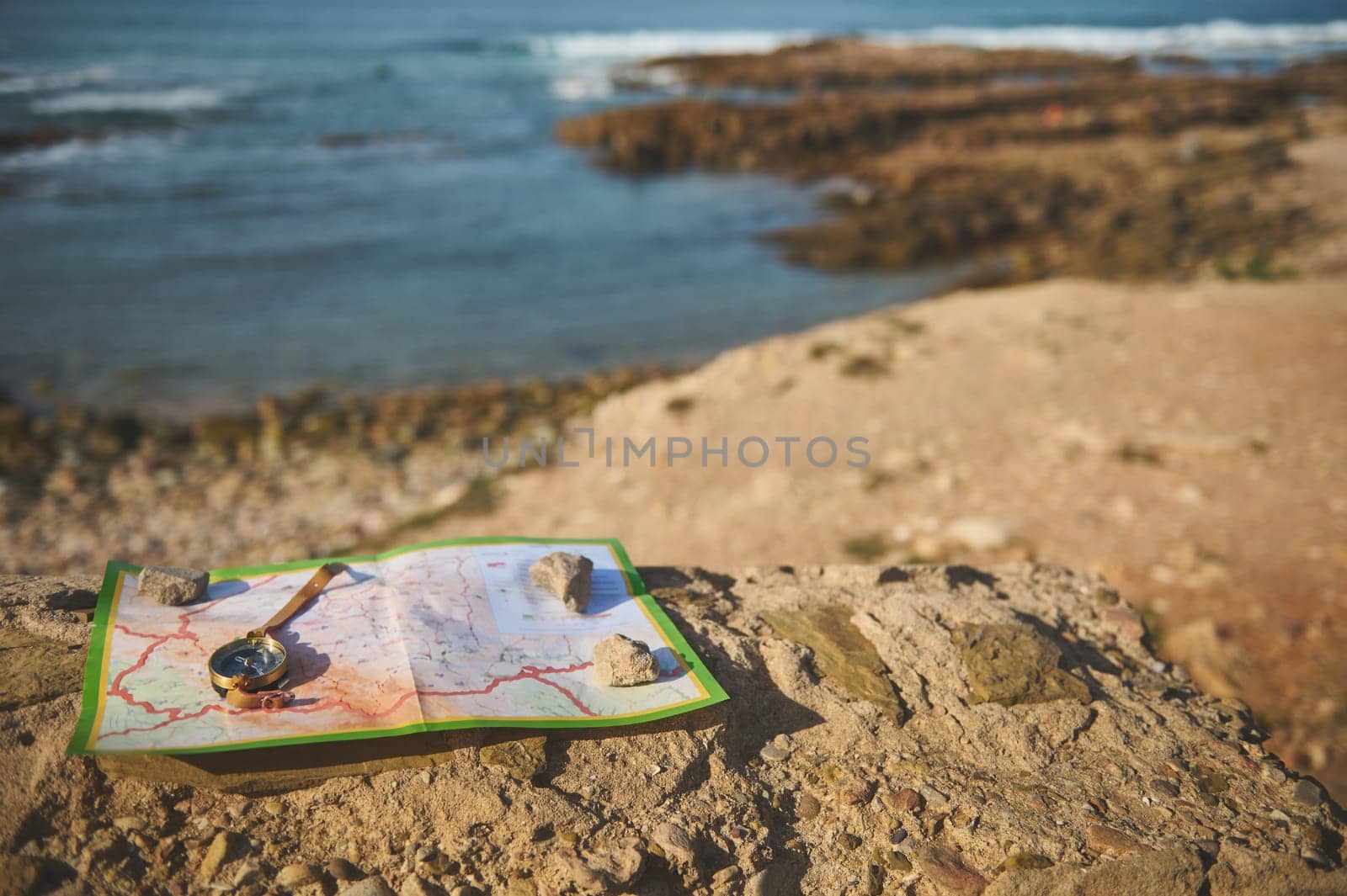 Still life with a golden compass on a geographic map lying down on the top of a rock overlooking seascape. Travel destinations. Trip. Journey.