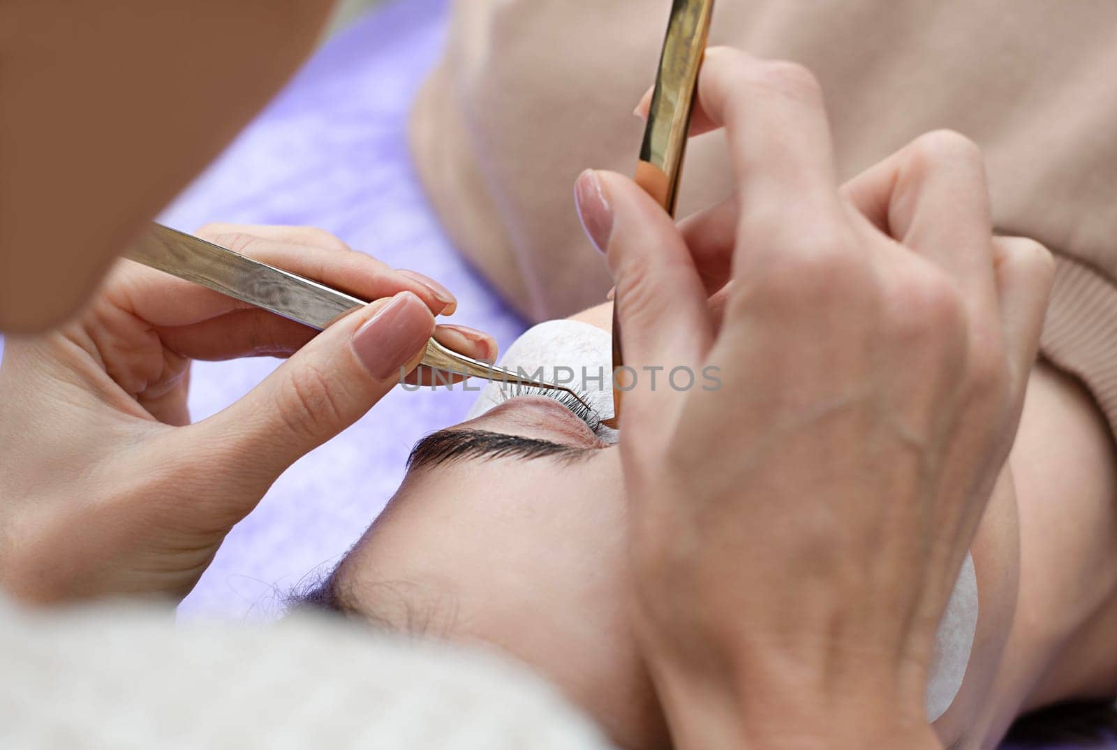 Beauty concept. Cosmetology. Eyelash extensions. A beautiful girl lies on the sofa in a beauty salon. A master, specialist does eyelash extensions on eyelashes. Close-up.