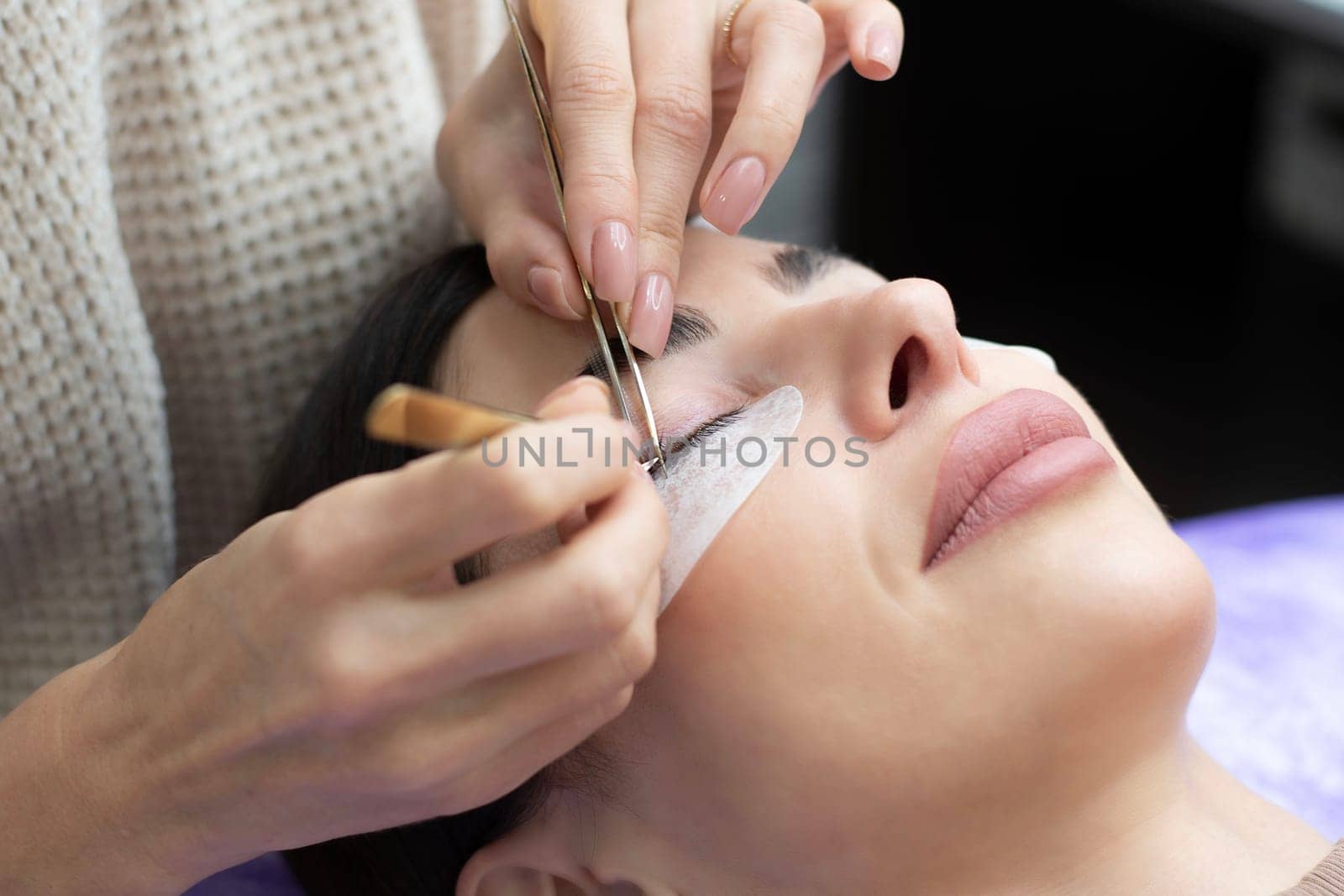 Beauty concept. Cosmetology. Eyelash extensions. A beautiful girl lies on the sofa in a beauty salon. A master, specialist does eyelash extensions on eyelashes. Close-up.