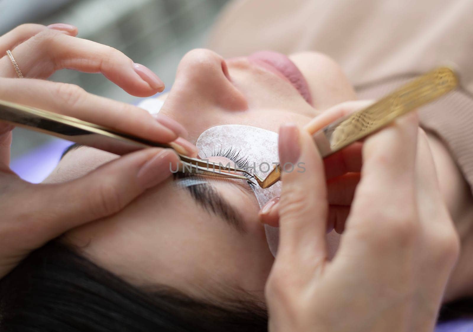 Beauty concept. Cosmetology. Eyelash extensions. A beautiful girl lies on the sofa in a beauty salon. A master, specialist does eyelash extensions on eyelashes. Close-up.
