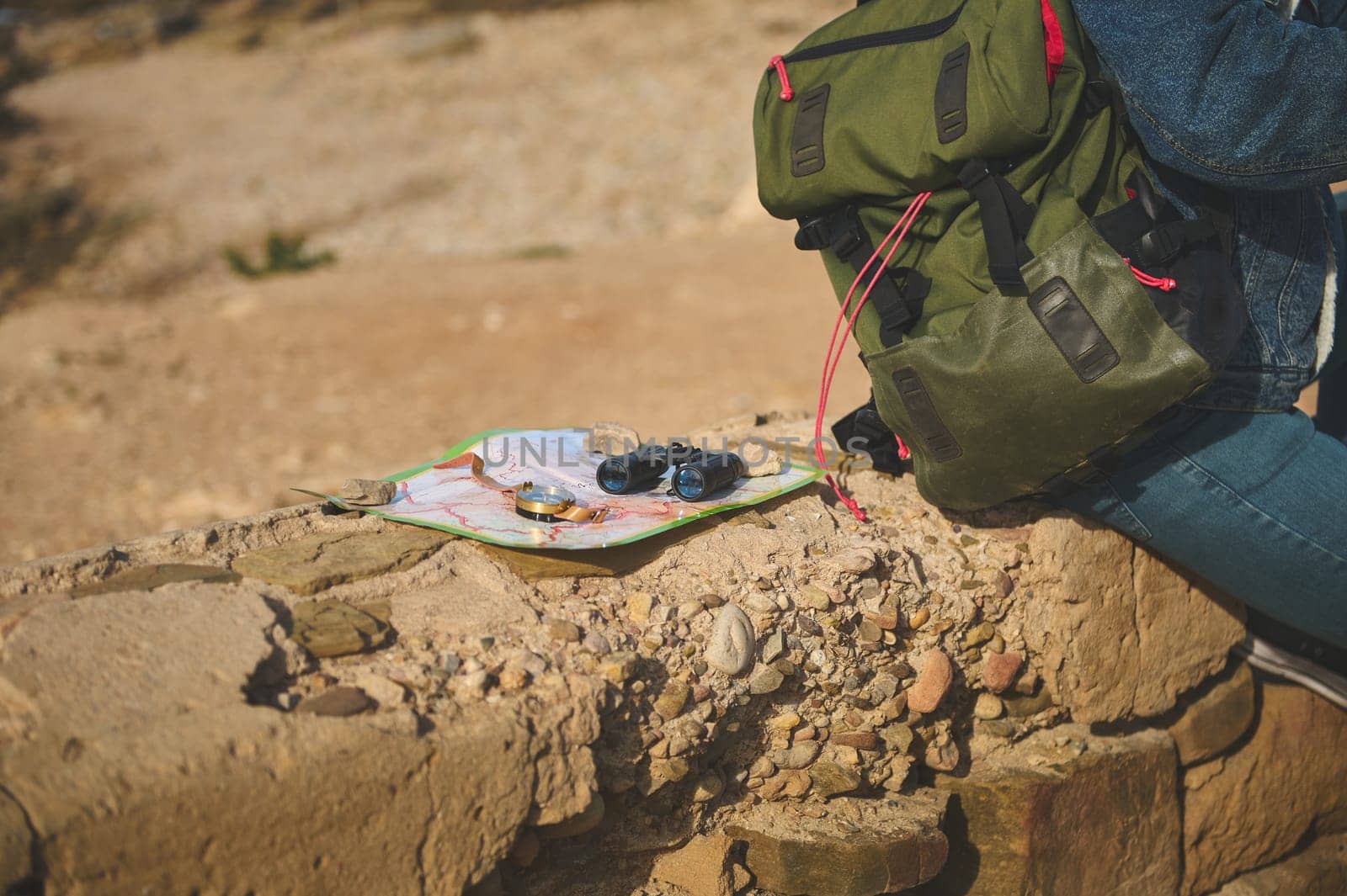 Binoculars, compass on map near backpack of a tourist sitting on the cliff, enjoying his hiking on the adventure travel. by artgf