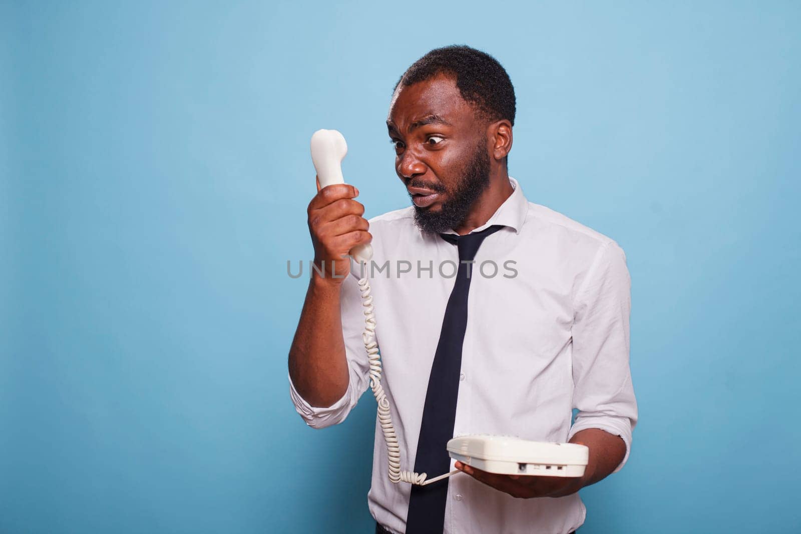 Angry black businessman yelling into cord phone receiver, arguing with person on the other end of the line. Anxious african american employee arguing with manager on the phone.