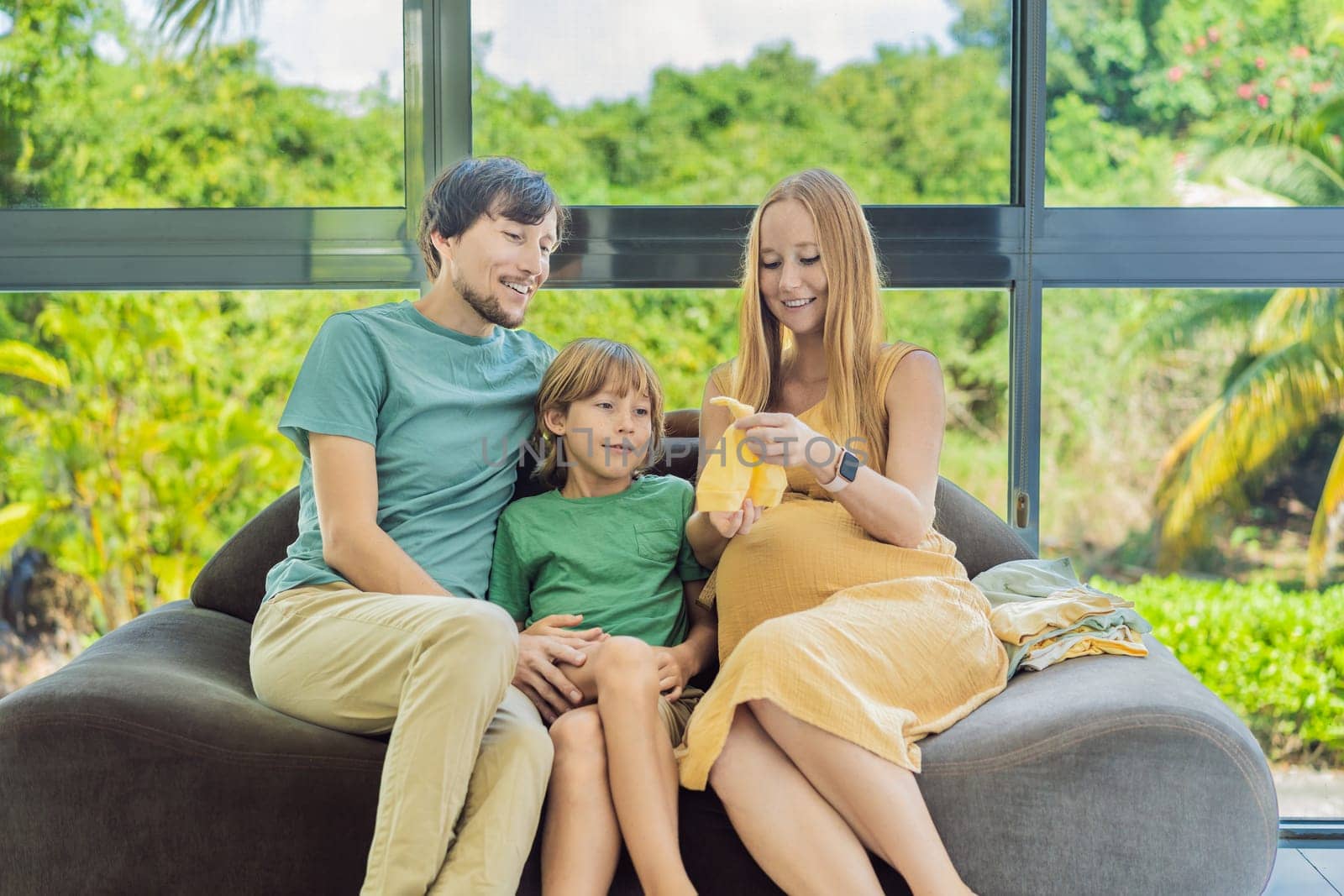 Heartwarming family moment as expectant mom, dad, and son joyfully browse through newborn baby's clothes, eagerly anticipating the arrival of a new family member by galitskaya