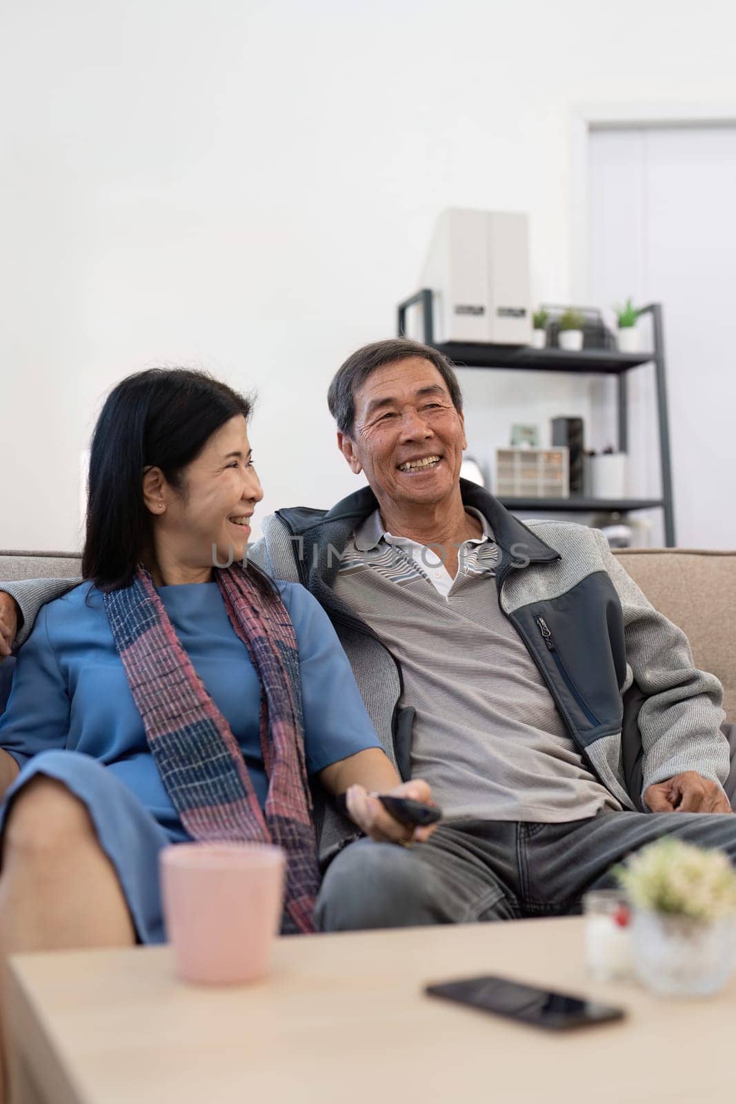 Asian senior couple enjoying in their favorite TV. Happy retirement couple watching television together in living room.