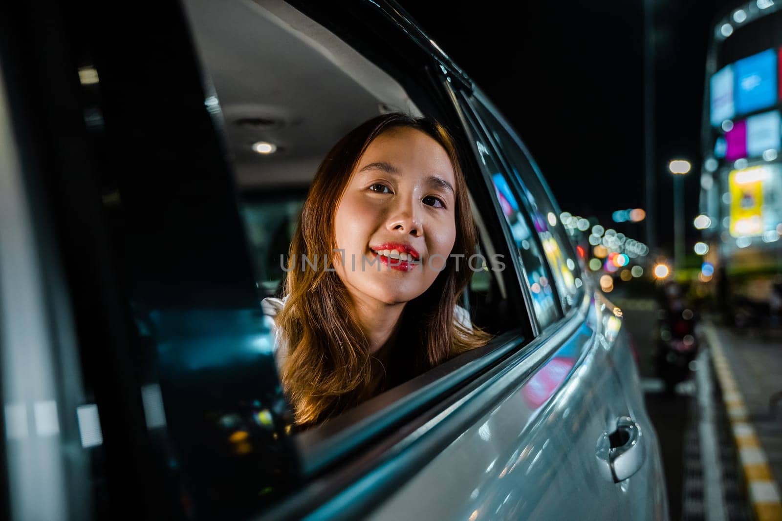 Traveling through the night city streets, the woman in the car gazes out the window at the scenery by Sorapop