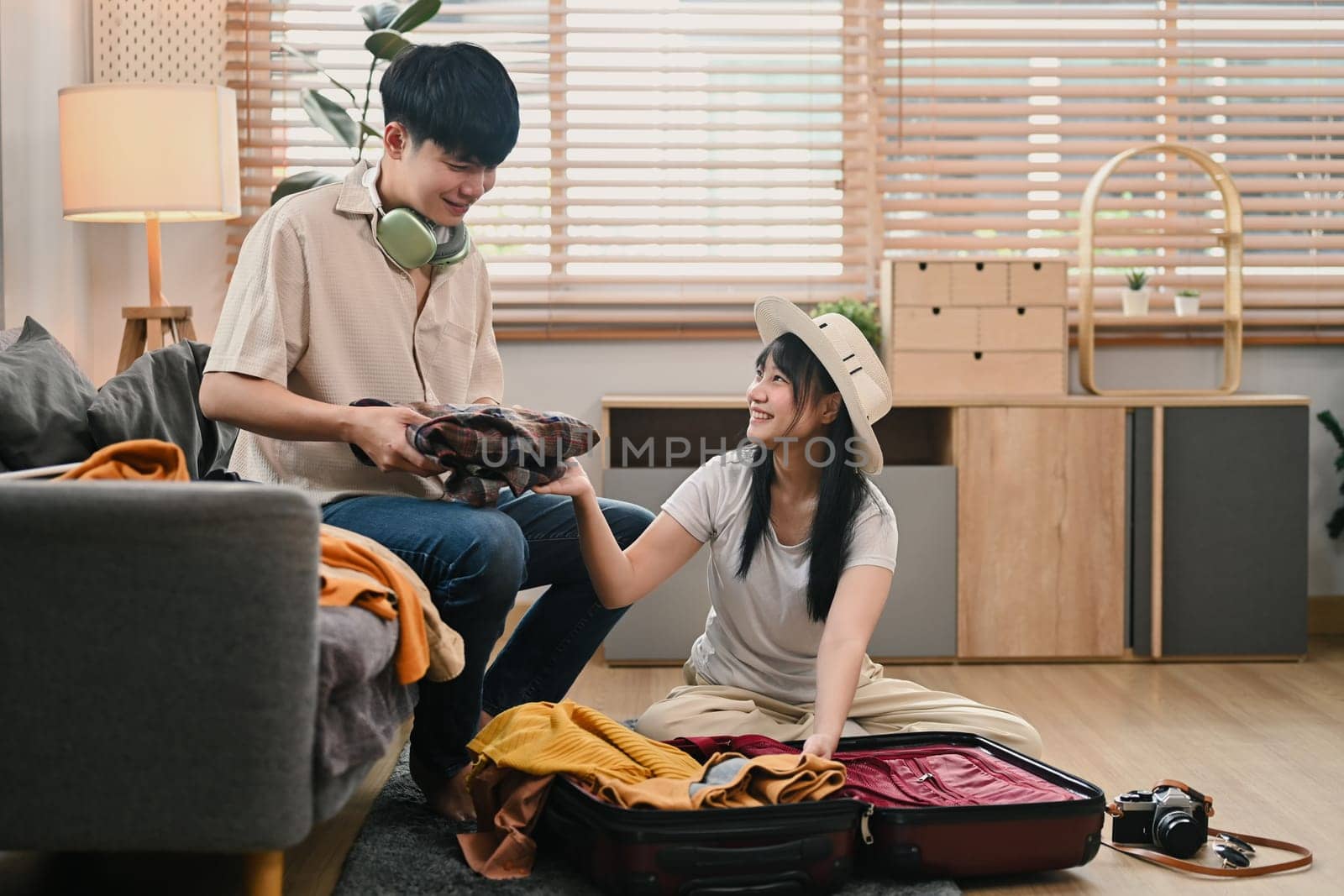 Shot of Asian couple packing clothes in the suitcase, preparing for vacation trip in living room.