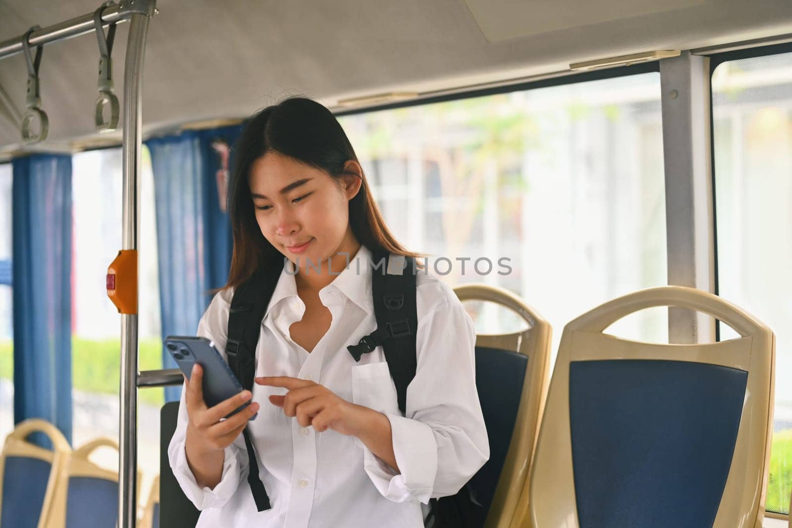 Smiling young woman text messaging on smart phone while traveling by bus. Public transportation concept.