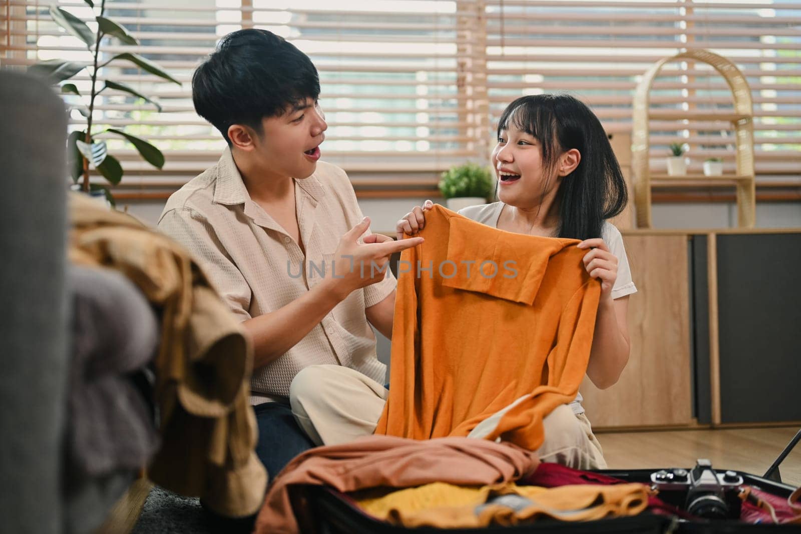 Excited tourists couple packing cloth and stuff for vacation trip in the living room at home.