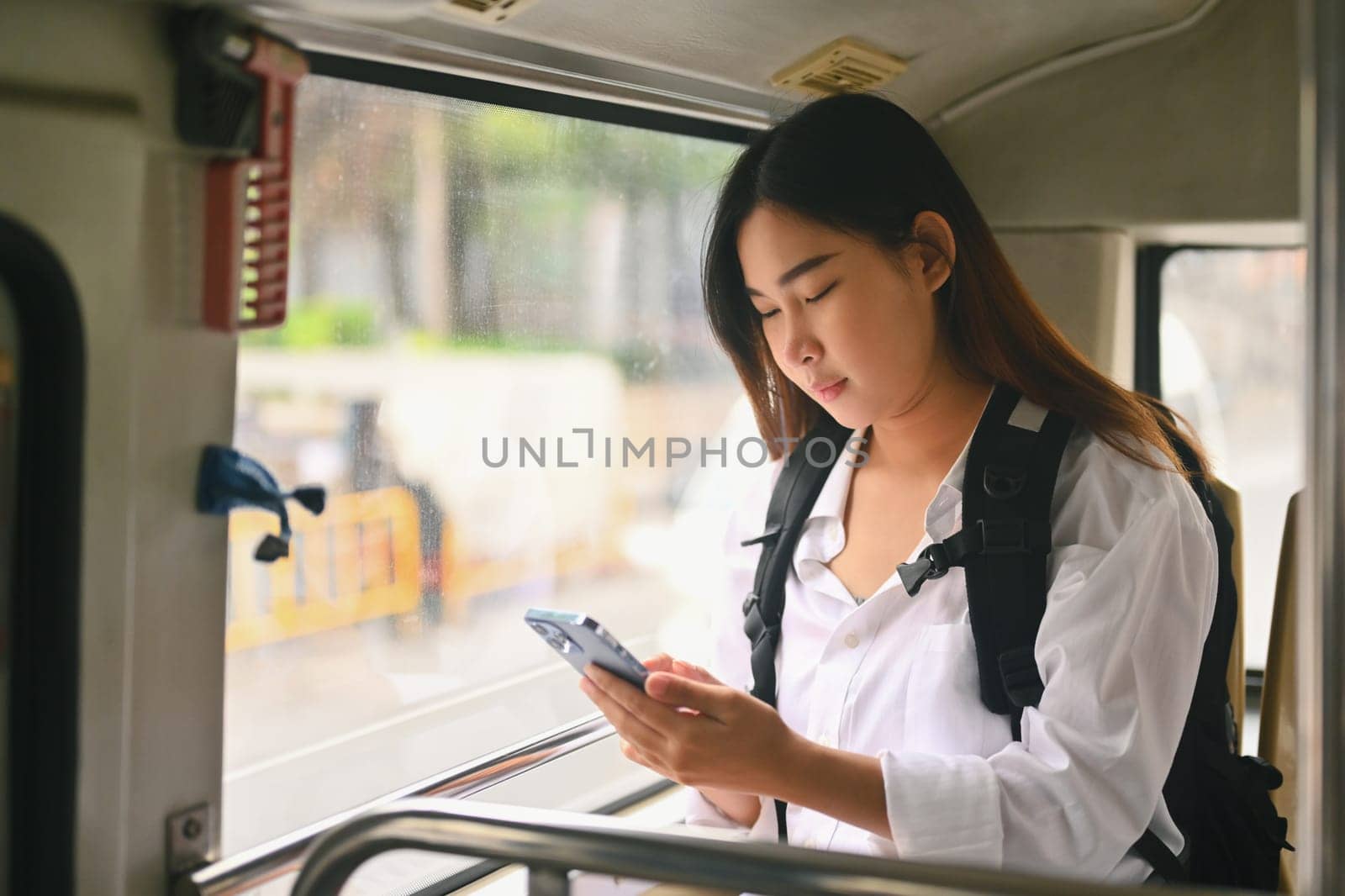 Young female commuter with backpack using mobile phone in public transportation.