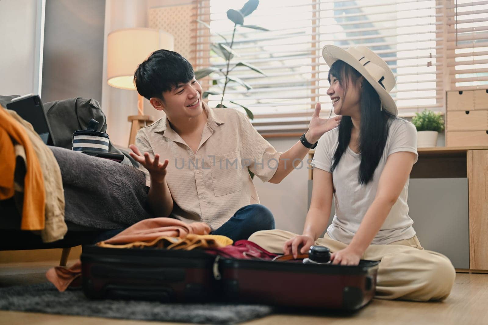 Cheerful young couple packing clothes in the suitcase, preparing for vacation trip in living room by prathanchorruangsak