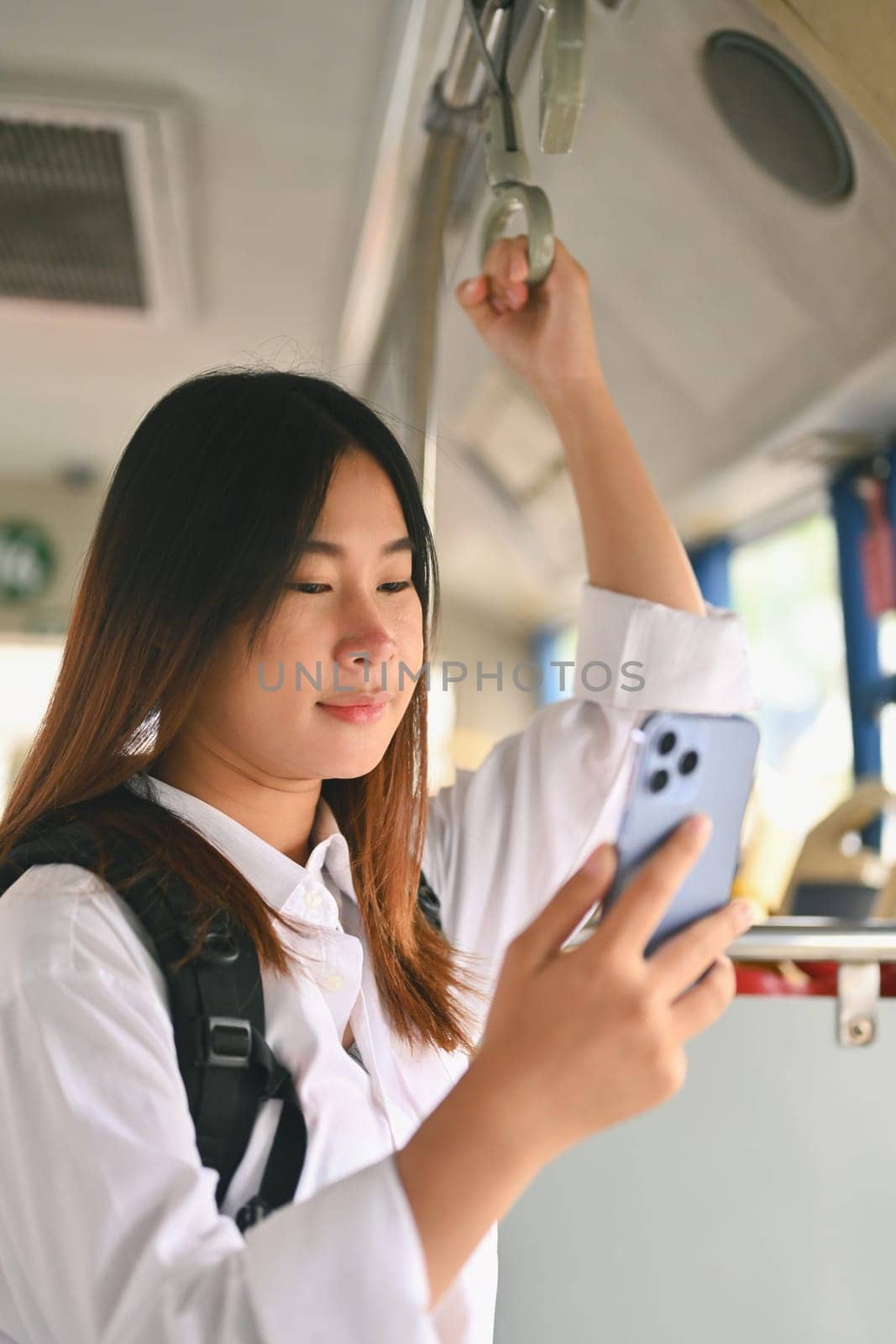 Portrait of young woman using a smartphone while standing on a bus. People and transportation concept.