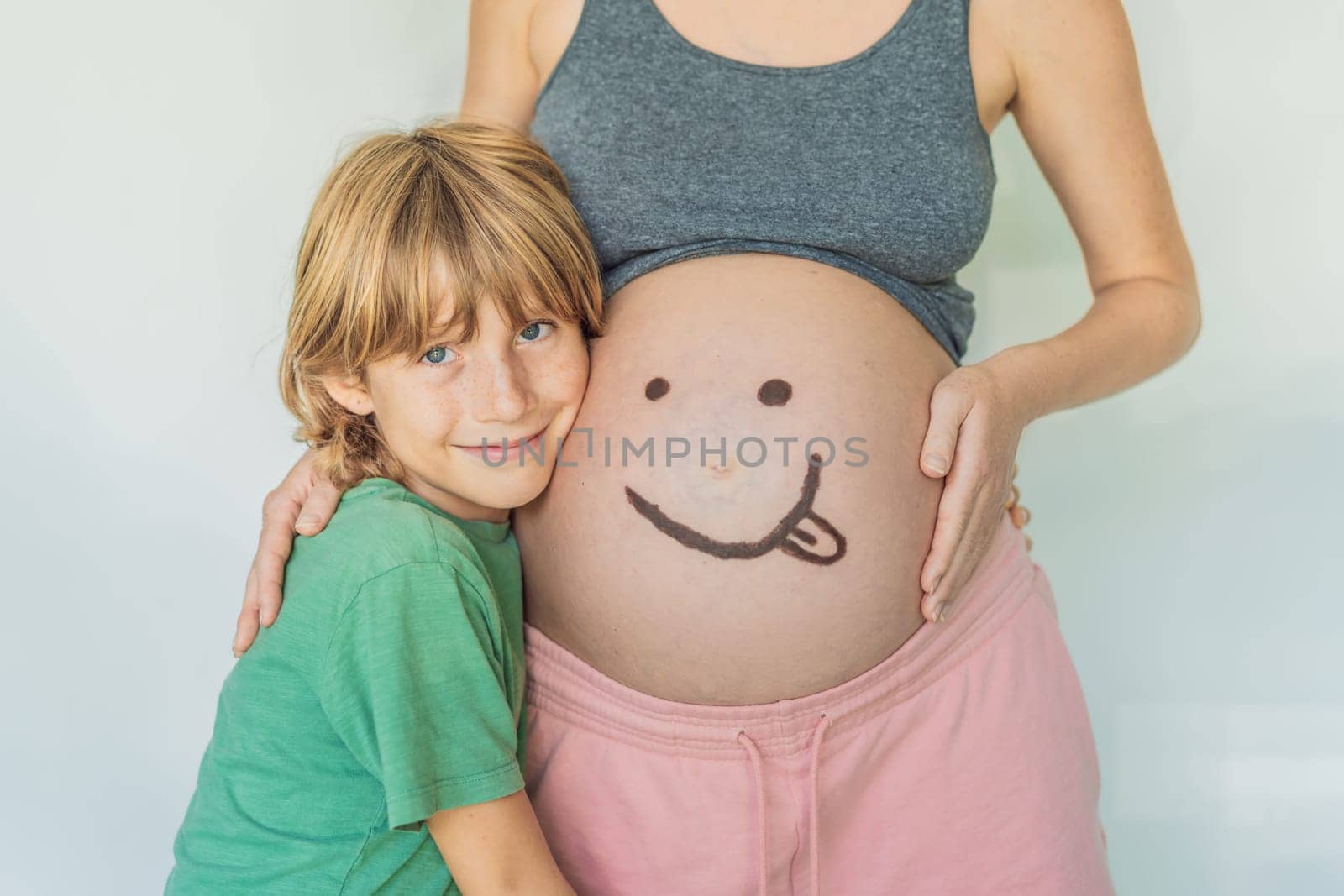 Adorable moment as a son adds a touch of joy to his mother's pregnancy, playfully drawing a funny face on her baby bump, creating cherished memories.