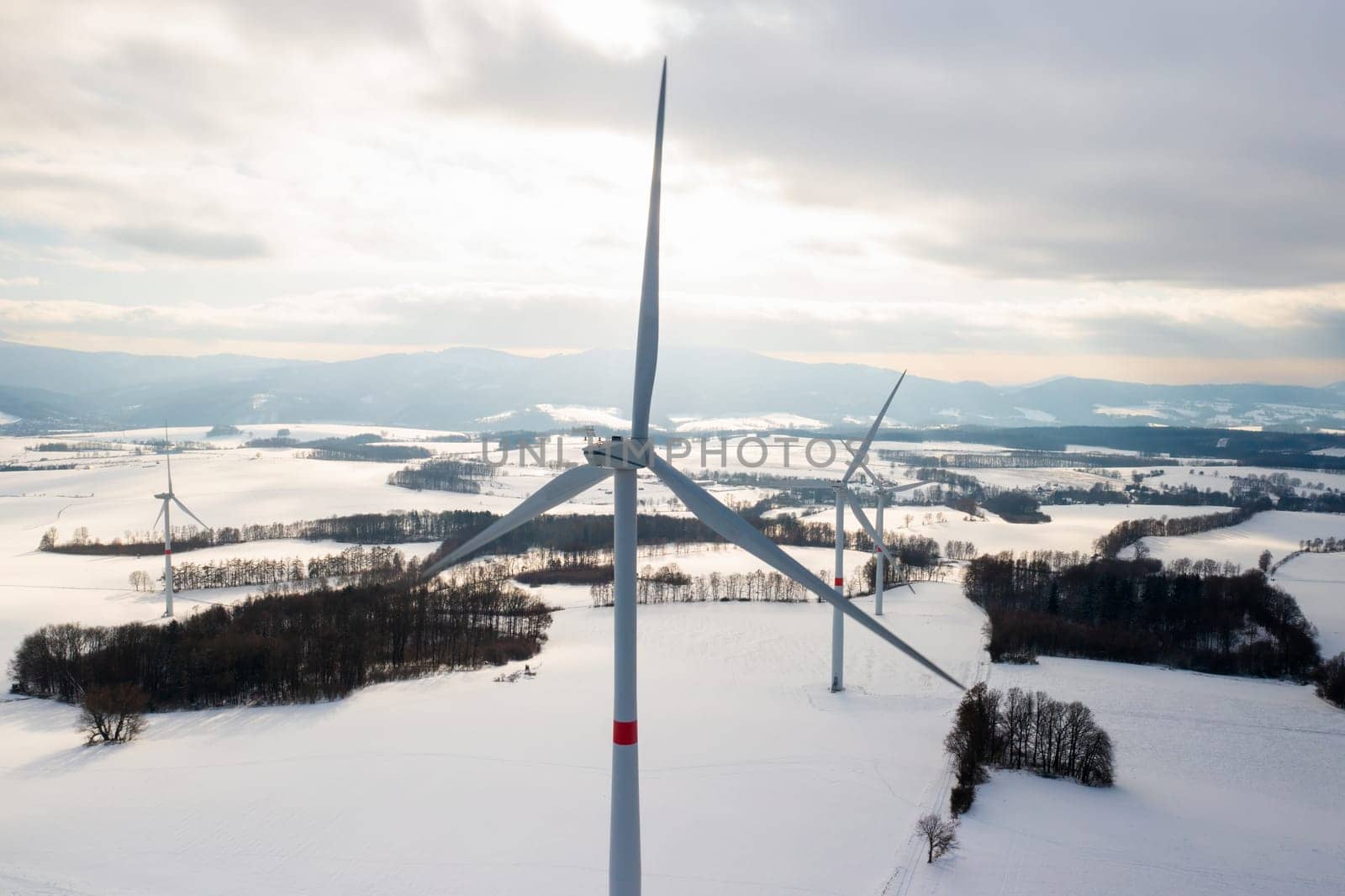 Fly over wind turbines and windmills in the winter field at sunlight. Clean and renewable energy sources concept.