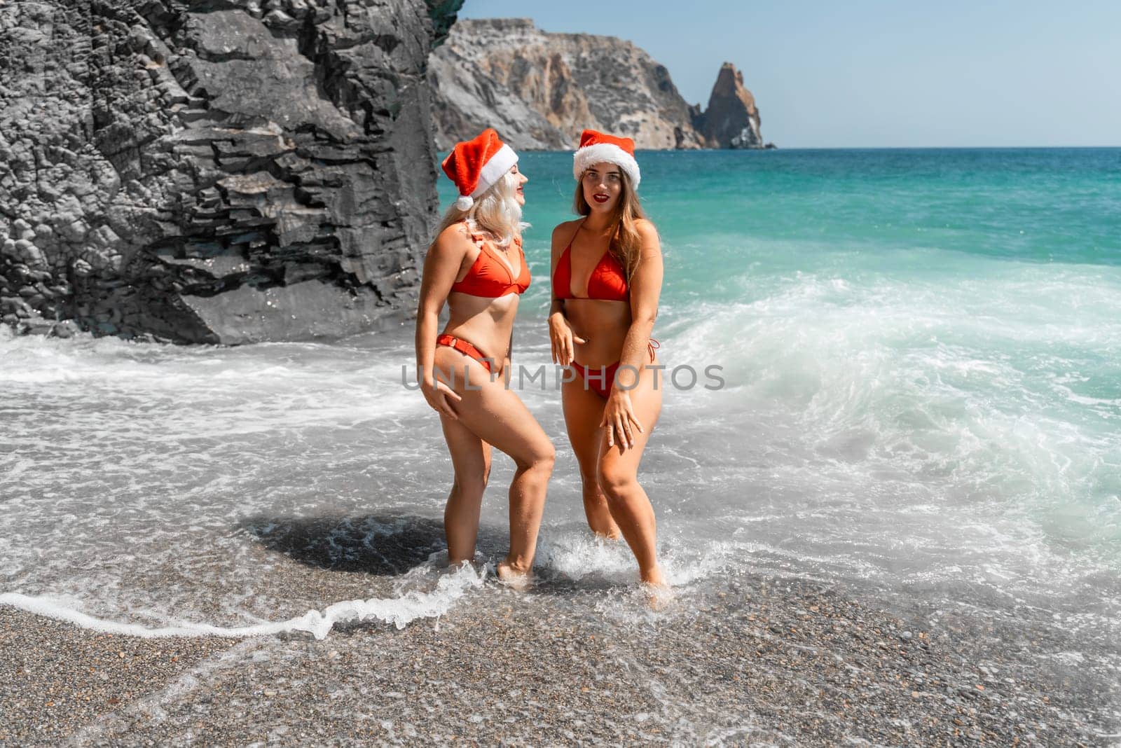 Women in Santa Claus hats run into the sea dressed in red swimsuits. Celebrating the New Year in a hot country.